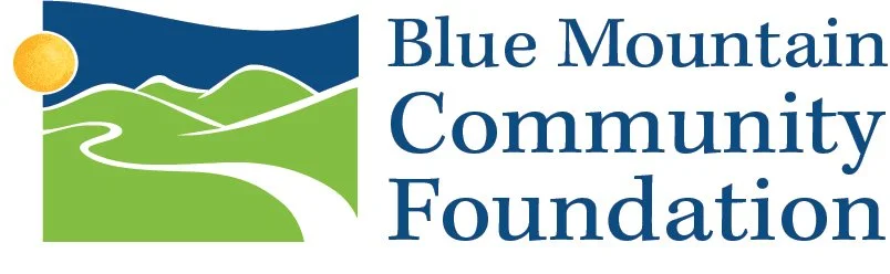 Logo of Blue Mountain Community Foundation featuring green hills, a white winding path, a yellow circle representing the sun, and the organization's name in blue text.