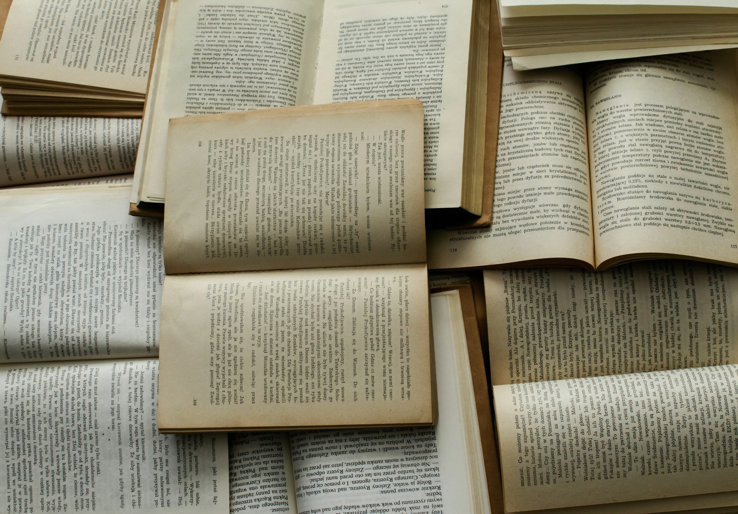Several open books with text in different languages, overlapping each other, laid out flat on a surface.