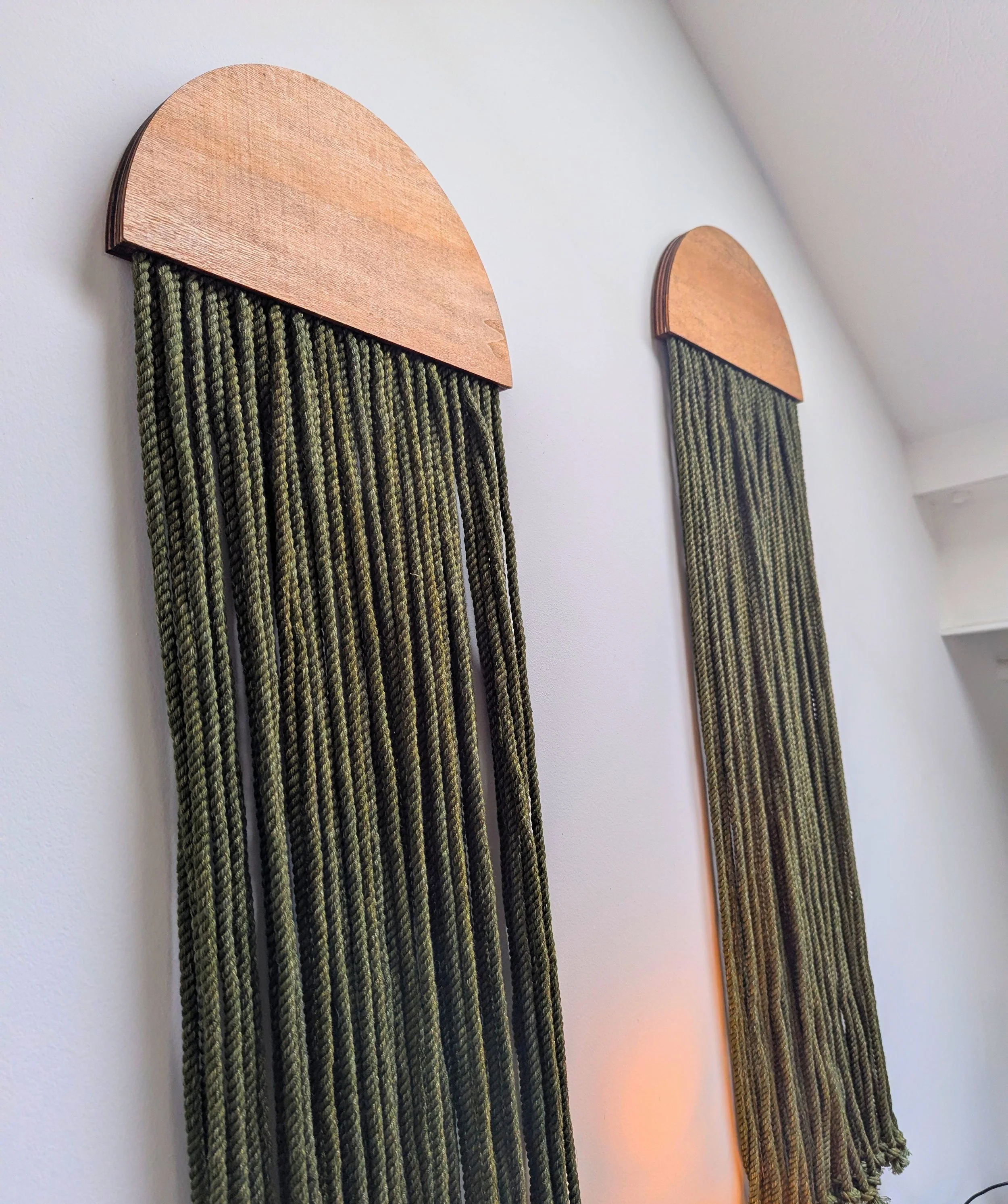 Two wall hanging decorations with wooden semi-circular tops and green and black striped tassels hanging below, mounted on a white wall.