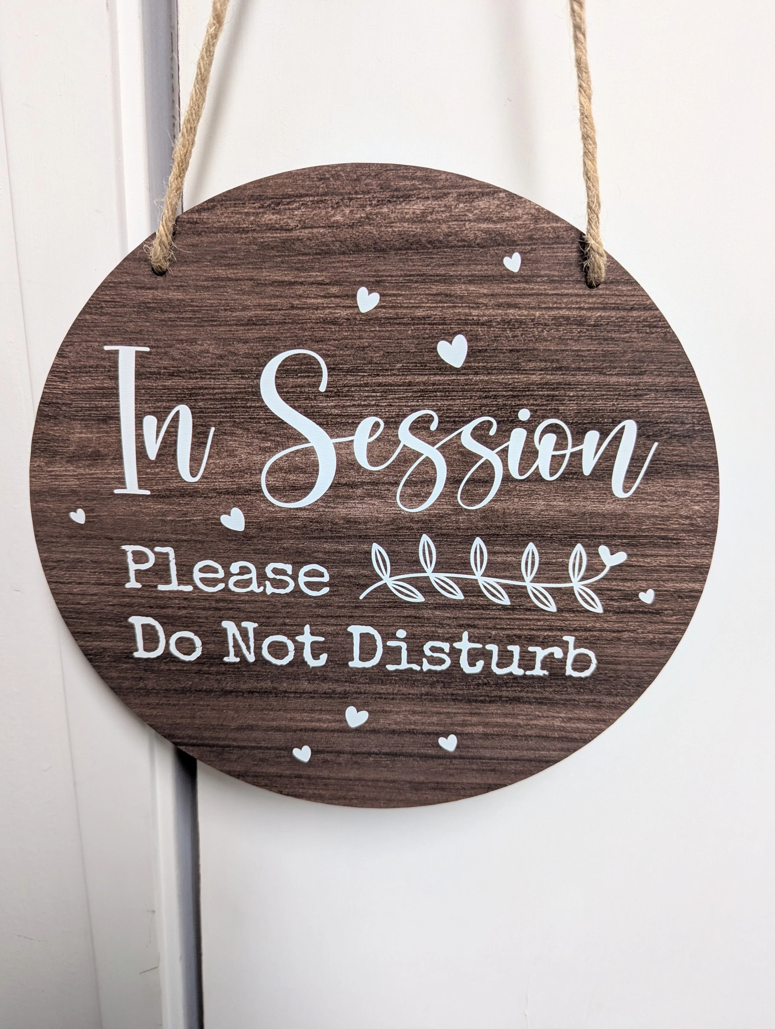 Round wooden sign with a rope hanger, decorated with small white hearts, and text that reads 'In Session Please Do Not Disturb'.