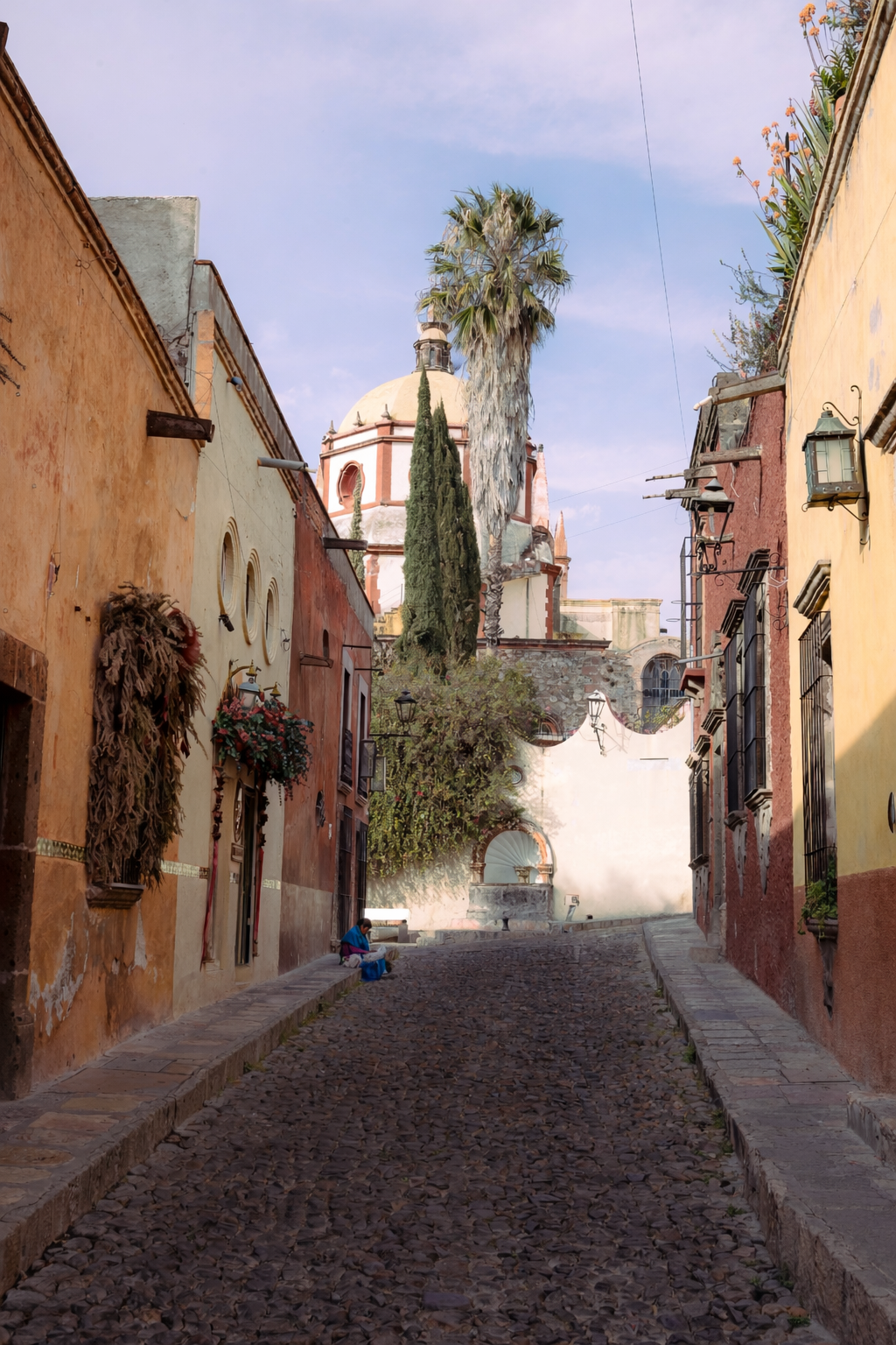 calles empedradas con edificios coloridos en una ciudad colonial mexicana, con una iglesia en el fondo y un árbol de palmera en el centro