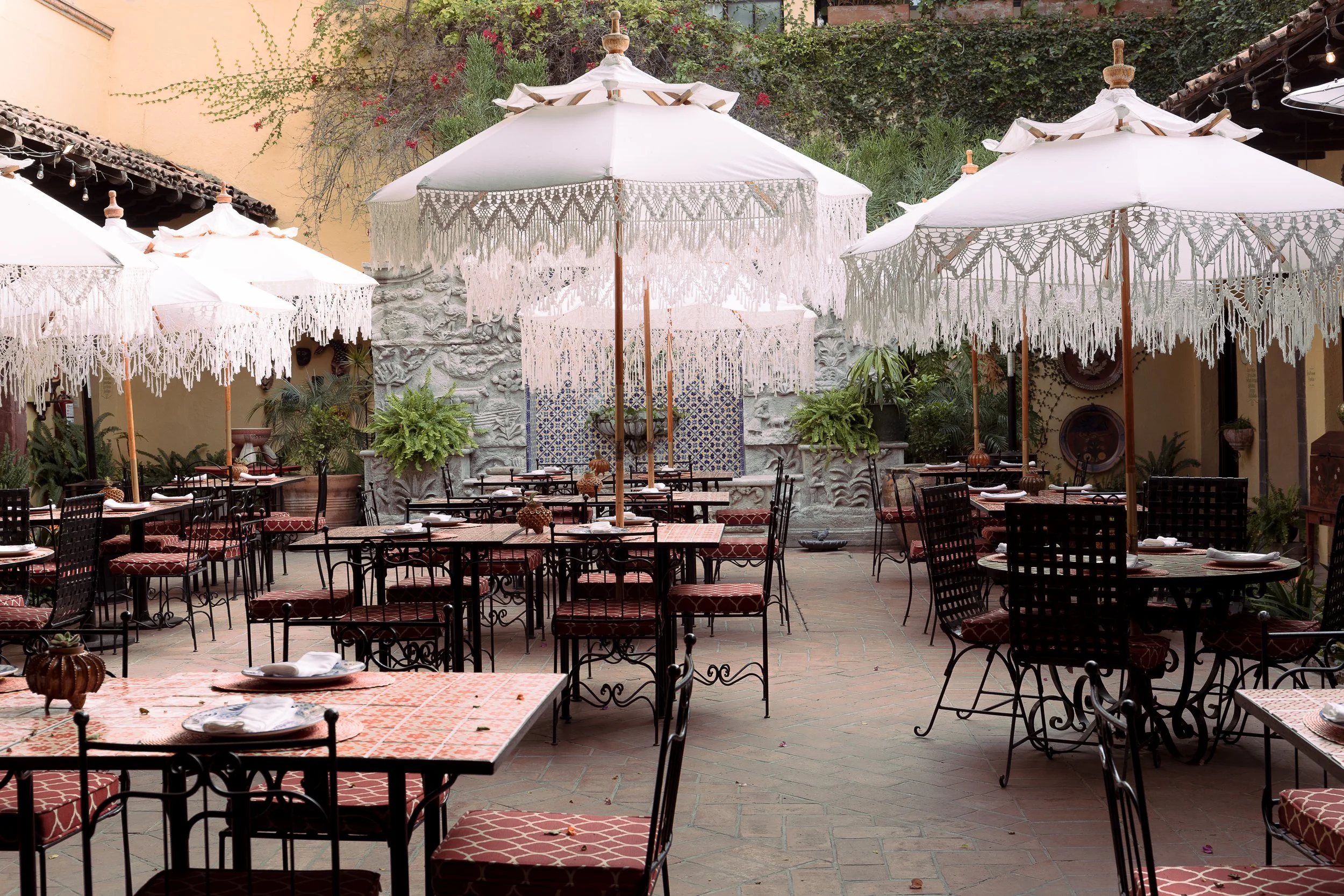 Terraza de restaurante con mesas, sillas, manteles y sombrillas blancas decorativas en un ambiente abierto
