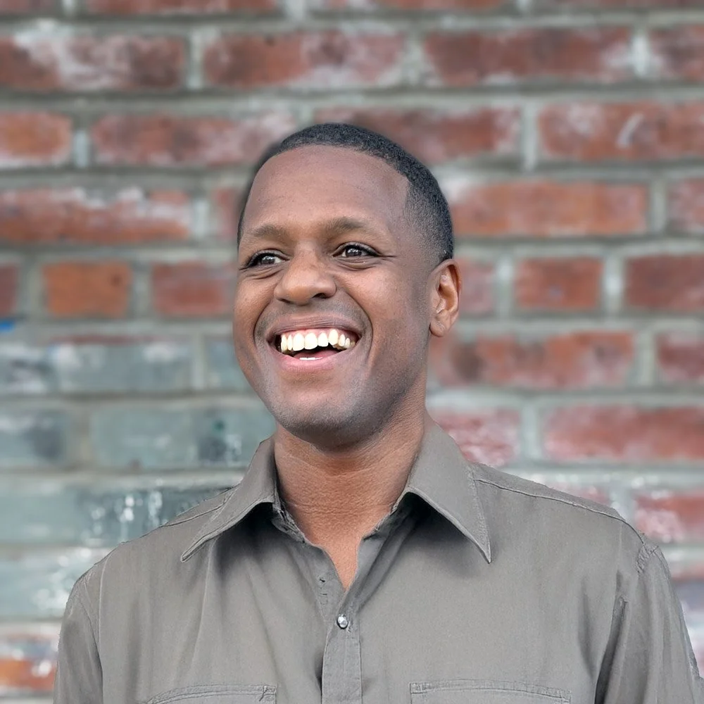 A man smiling with a brick wall in the background.