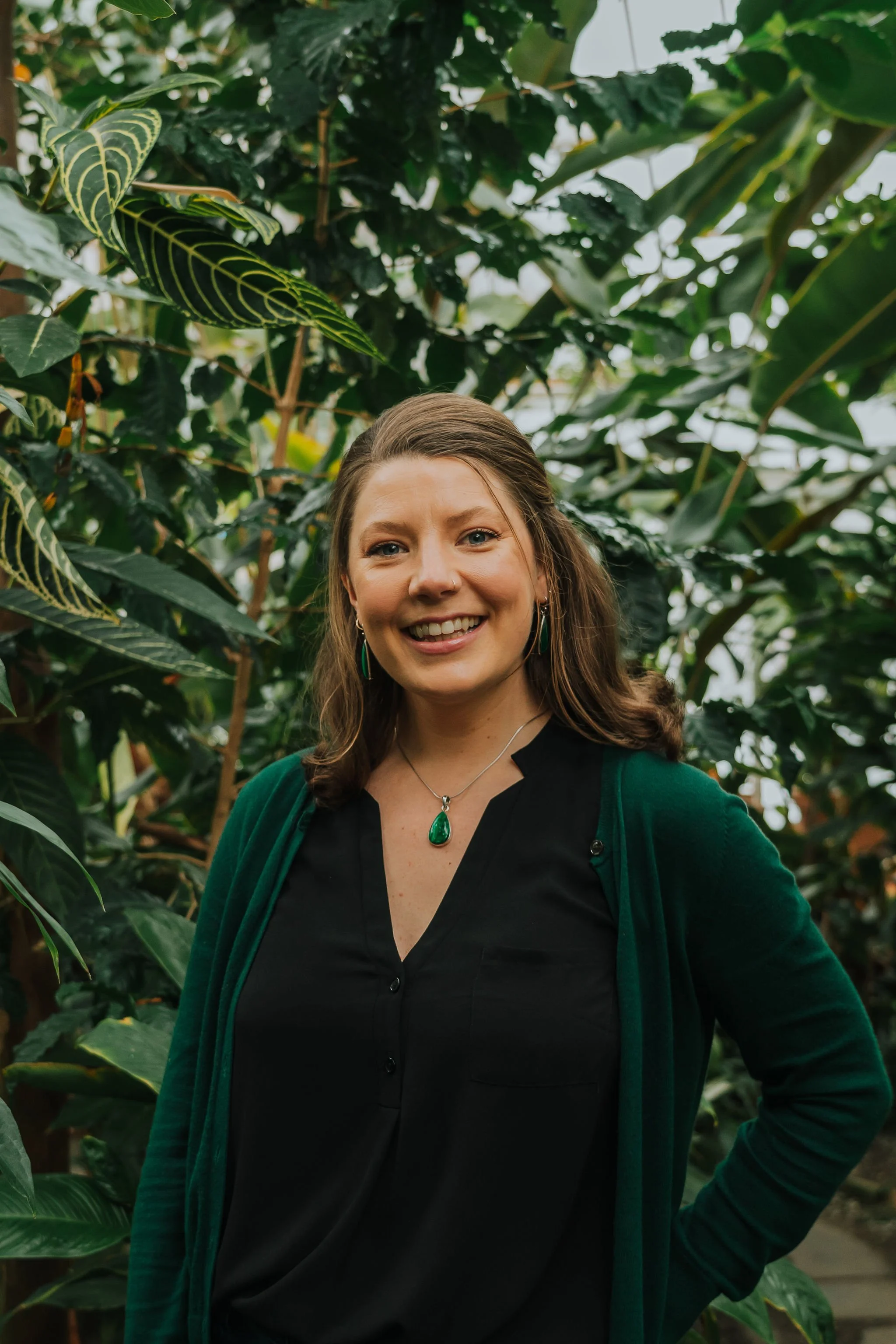 A woman smiling in a greenhouse surrounded by lush green plants.