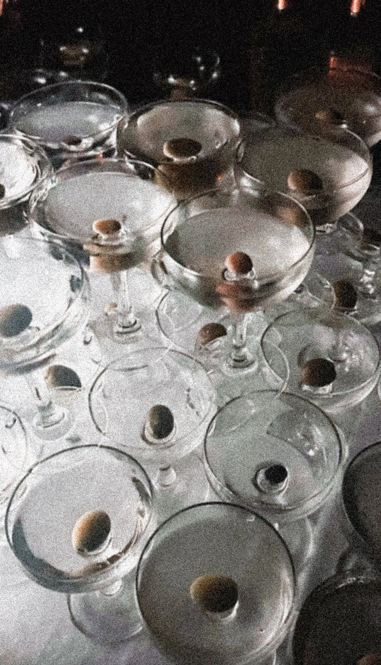 Multiple cocktail glasses with a cherry garnish, arranged on a reflective surface.