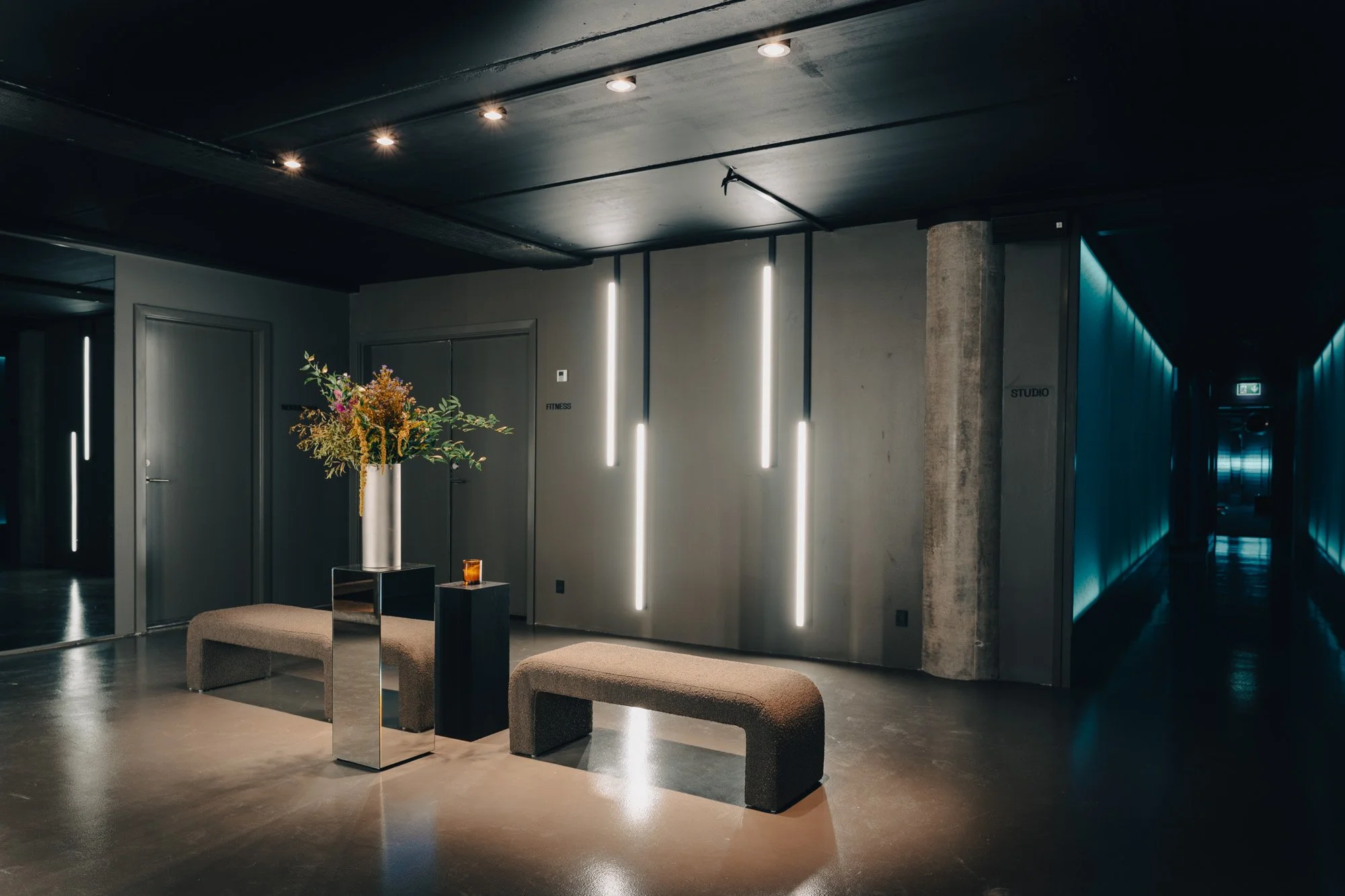 Modern, dimly lit lobby with benches, a flower arrangement, and vertical LED light strips on the wall.