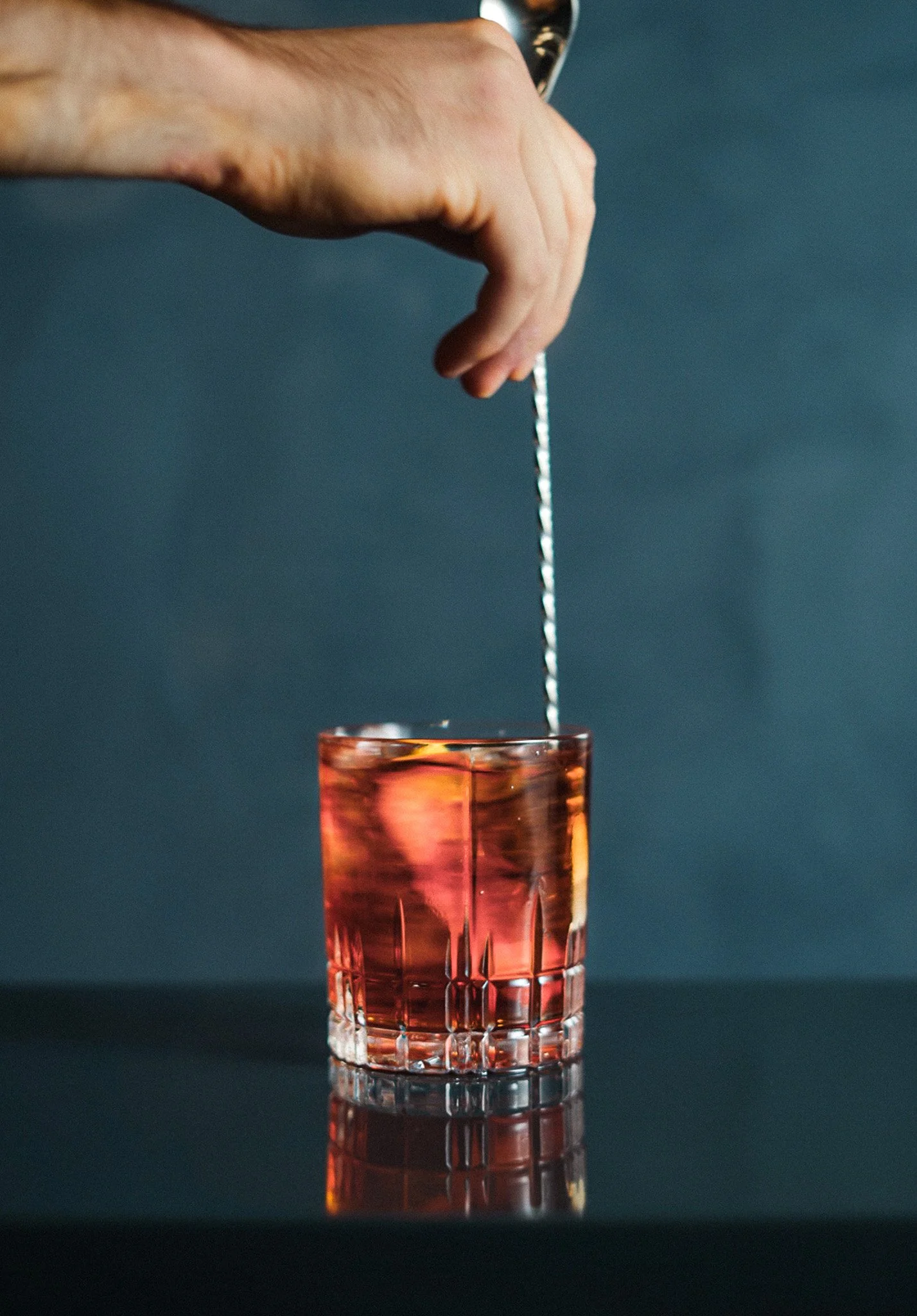 Hand dropping a metal straw into a glass of pink cocktail or drink.