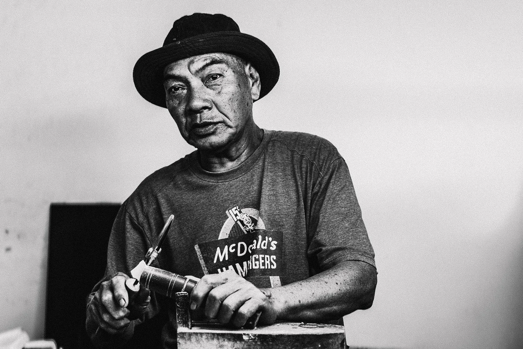 A black and white photo of an elderly man wearing a hat and a t-shirt sitting at a table, holding a Royal typewriter."