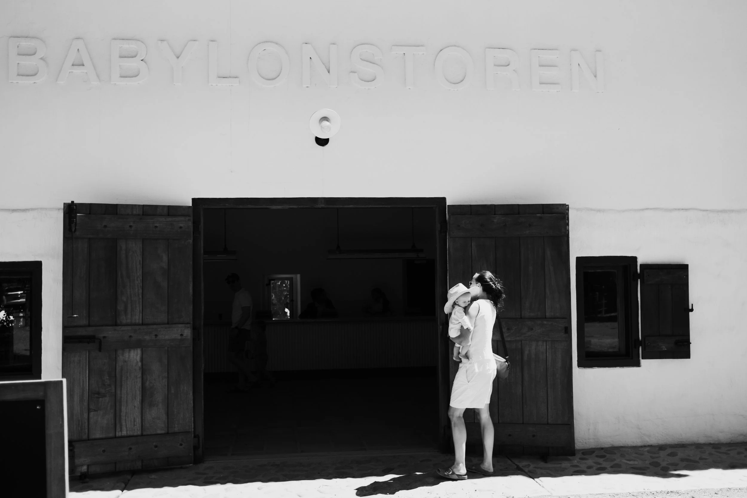 Woman holding a child outside a building with the sign 'BABYLONSTOREN' above the entrance, in black and white.