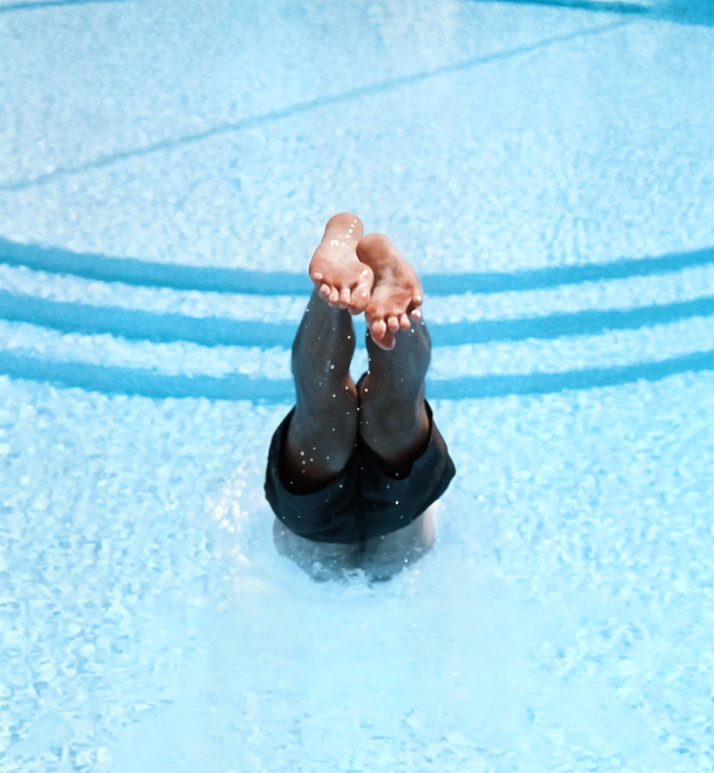 Person diving into a swimming pool with their legs and feet visible, water splashing around.
