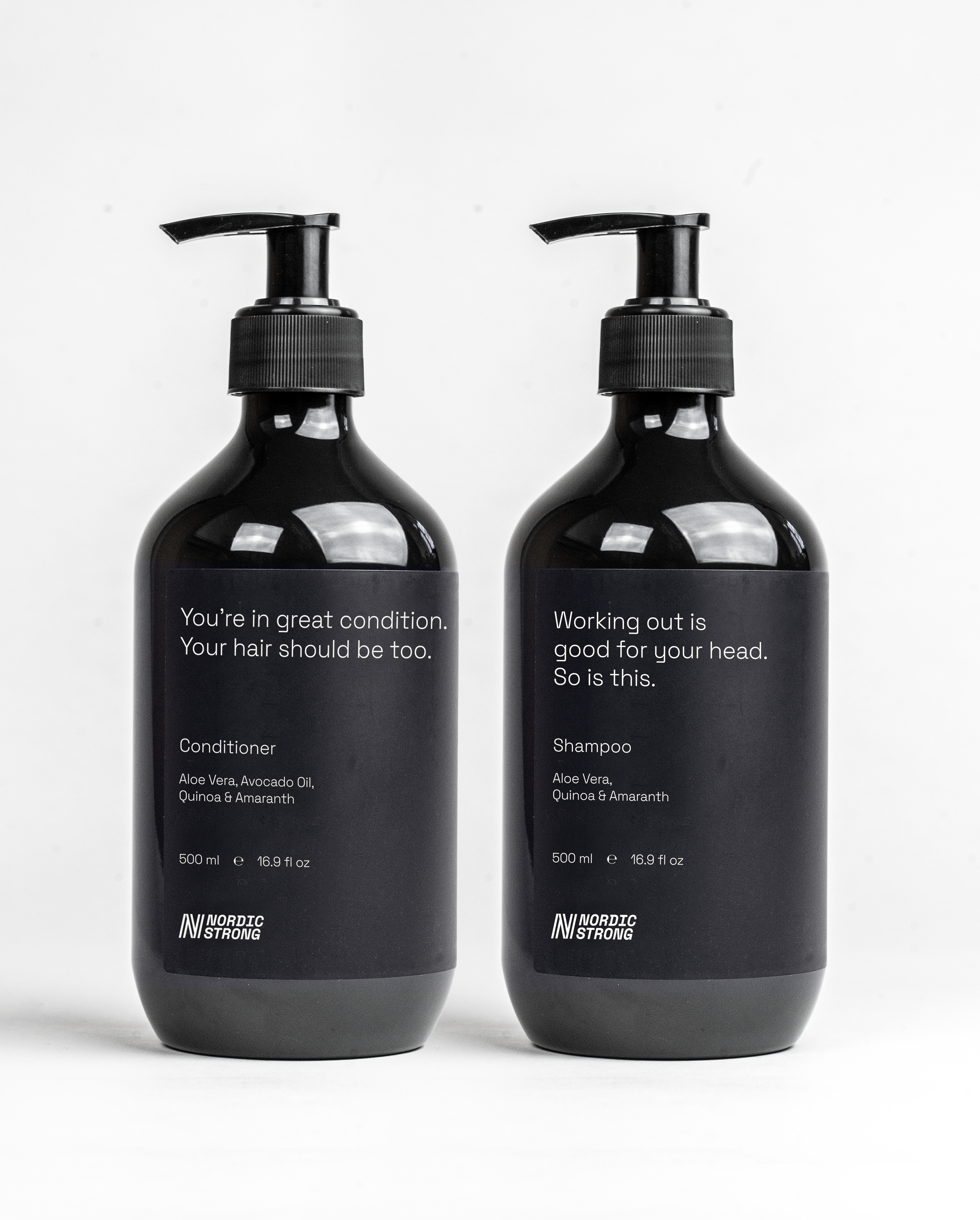Two black bottles with pump dispensers, labeled as conditioner and shampoo, on a white background. The conditioner bottle on the left says "You're in great condition. Your hair should be too. Aloe Vera, Avocado Oil, Quinoa & Amaranth. 500 ml, 16.9 fl