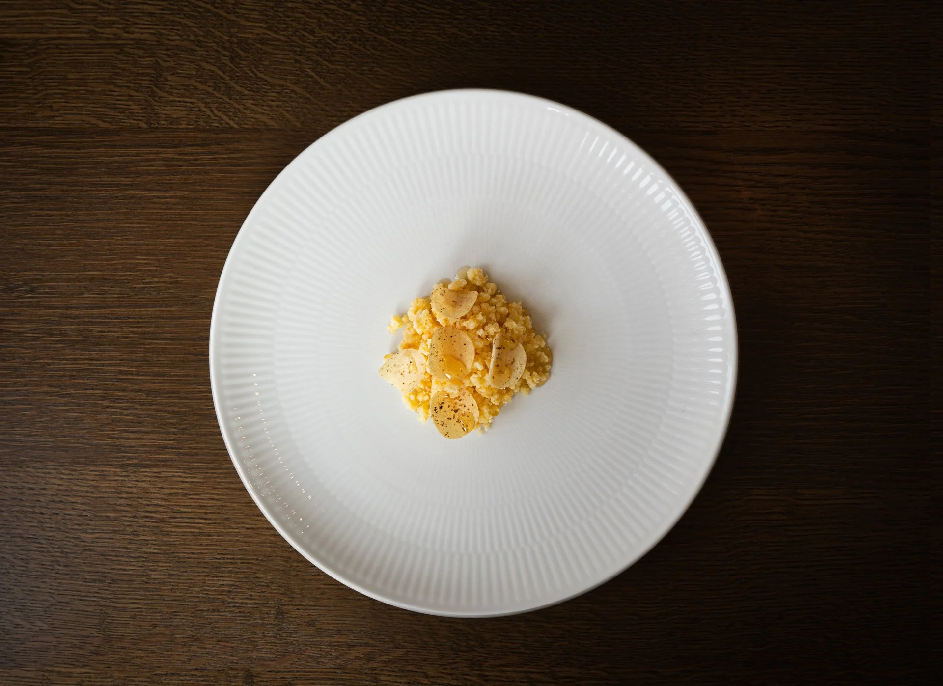 A white plate with a small portion of yellowish crumble topped with sliced almonds, placed on a dark wooden surface.