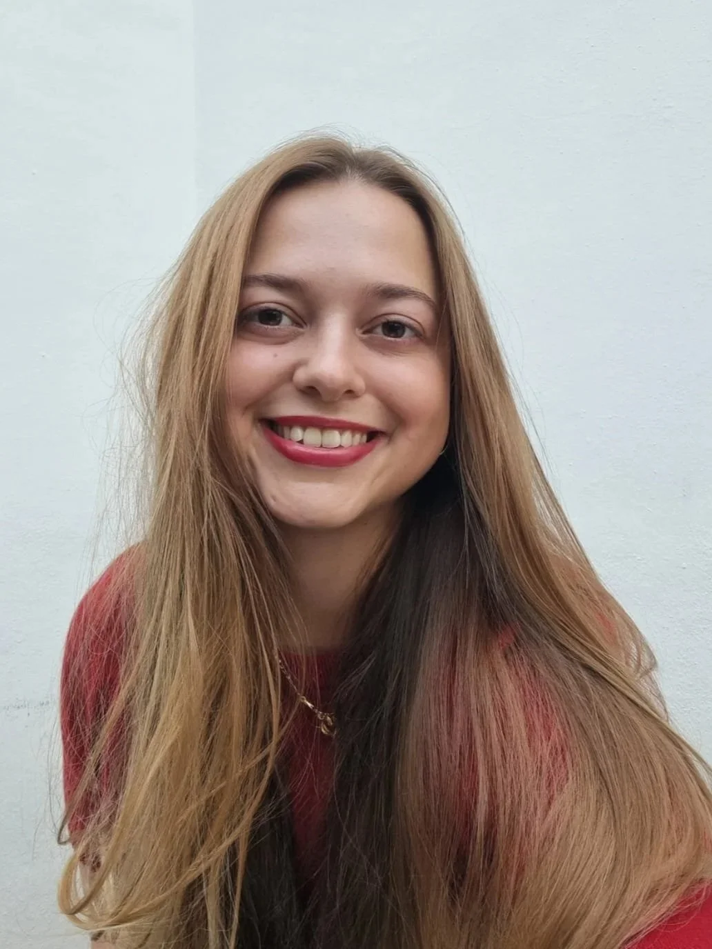 Retrato de una mujer joven con cabello largo y rubio, sonriendo, con fondo blanco