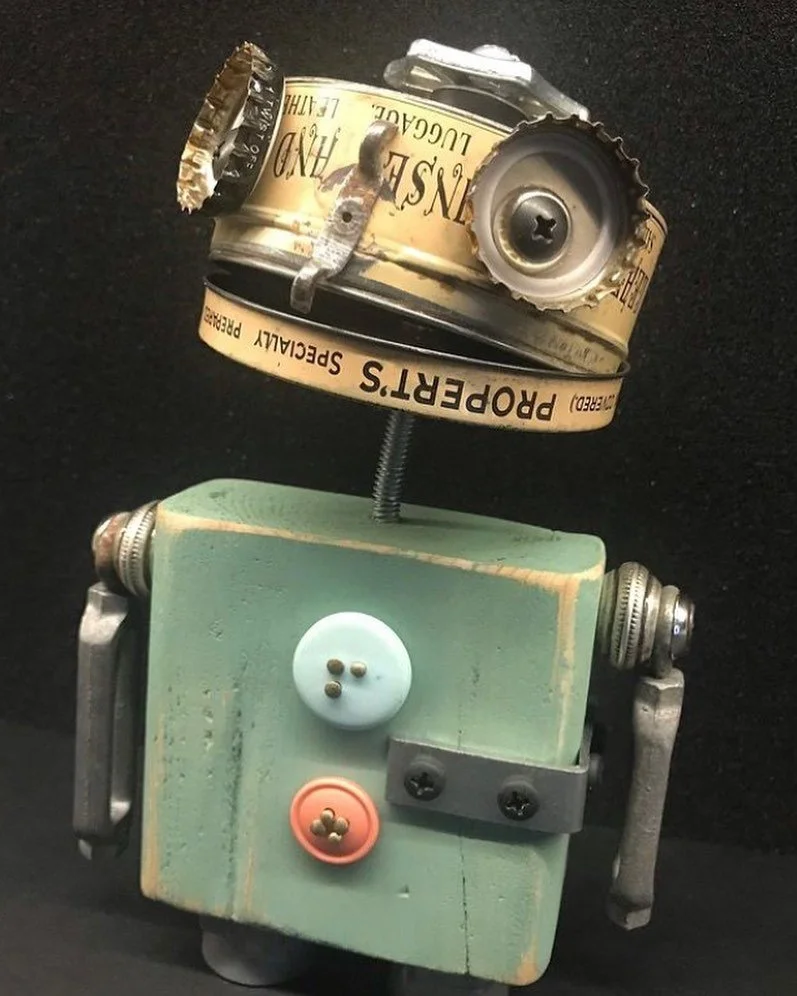 A robot made from various objects including a tin can, buttons, and hardware parts, with a black background.