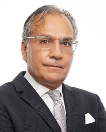 Retrato de un hombre con gafas, traje oscuro y corbata plateada.