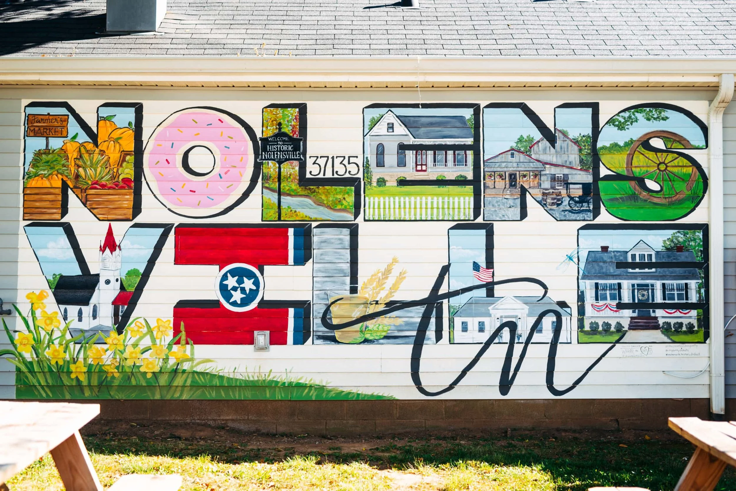 Colorful mural on a wall featuring the word 'NOLENS' with illustrations of a farmer's market, a donut, a house, a barn, a wheel, and flowers, with the phrase 'Welcome to Historic Nolensville' and the number 37135.