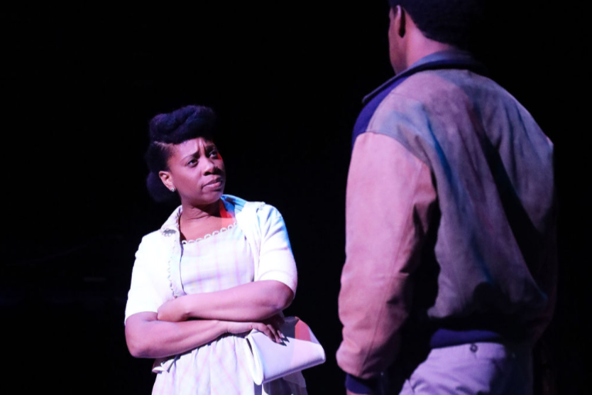 Two actors on stage engage in a scene, with the woman appearing concerned and the man facing away from the camera.
