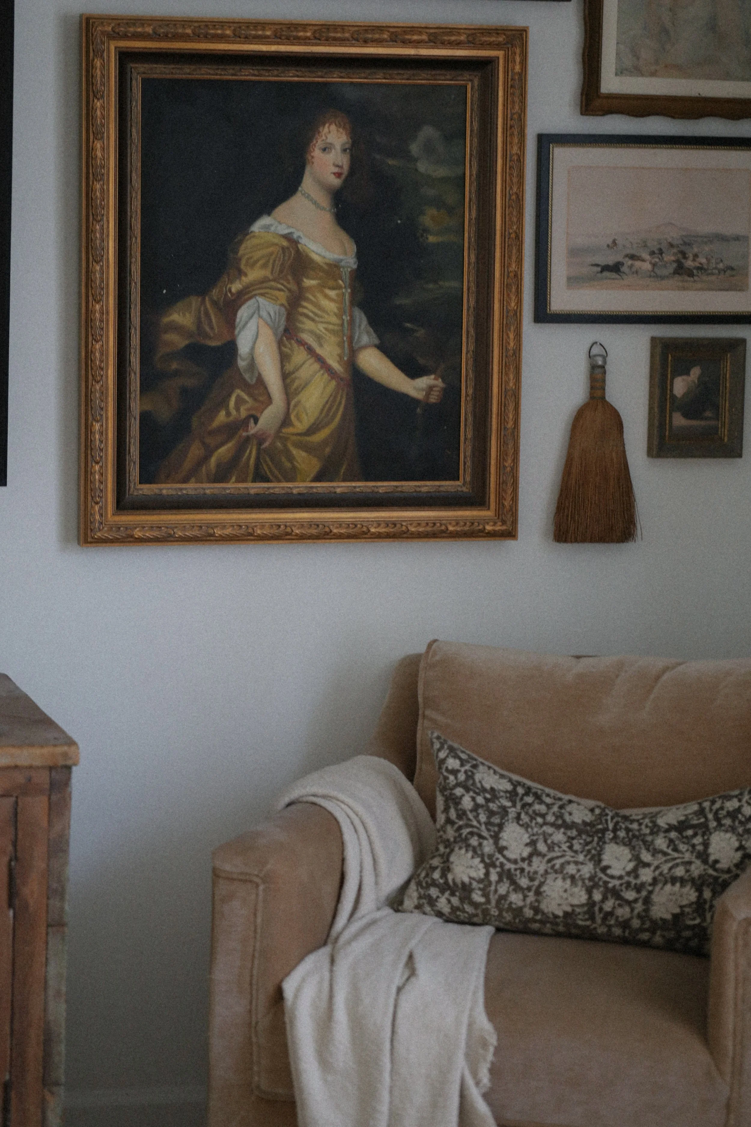 unique art gallery on wall with taupe velvet accent chair in front featuring a block print pillow and cream blanket