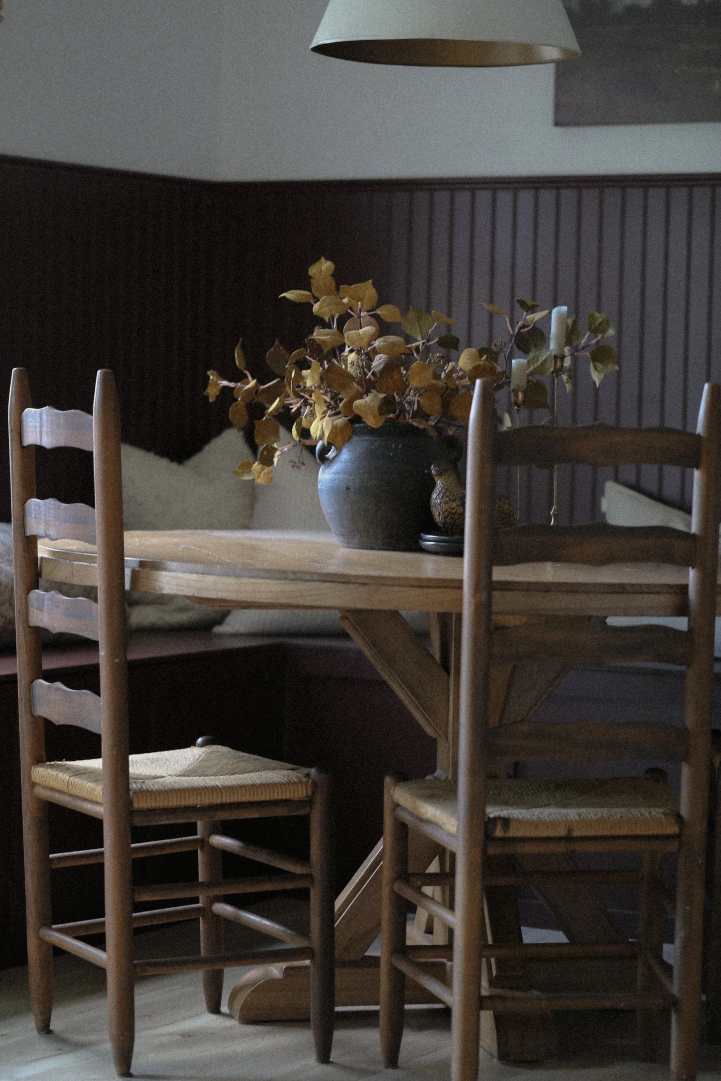 Burgundy dining nook with antique ladder back chairs. Pot and candlesticks on the dining table surface