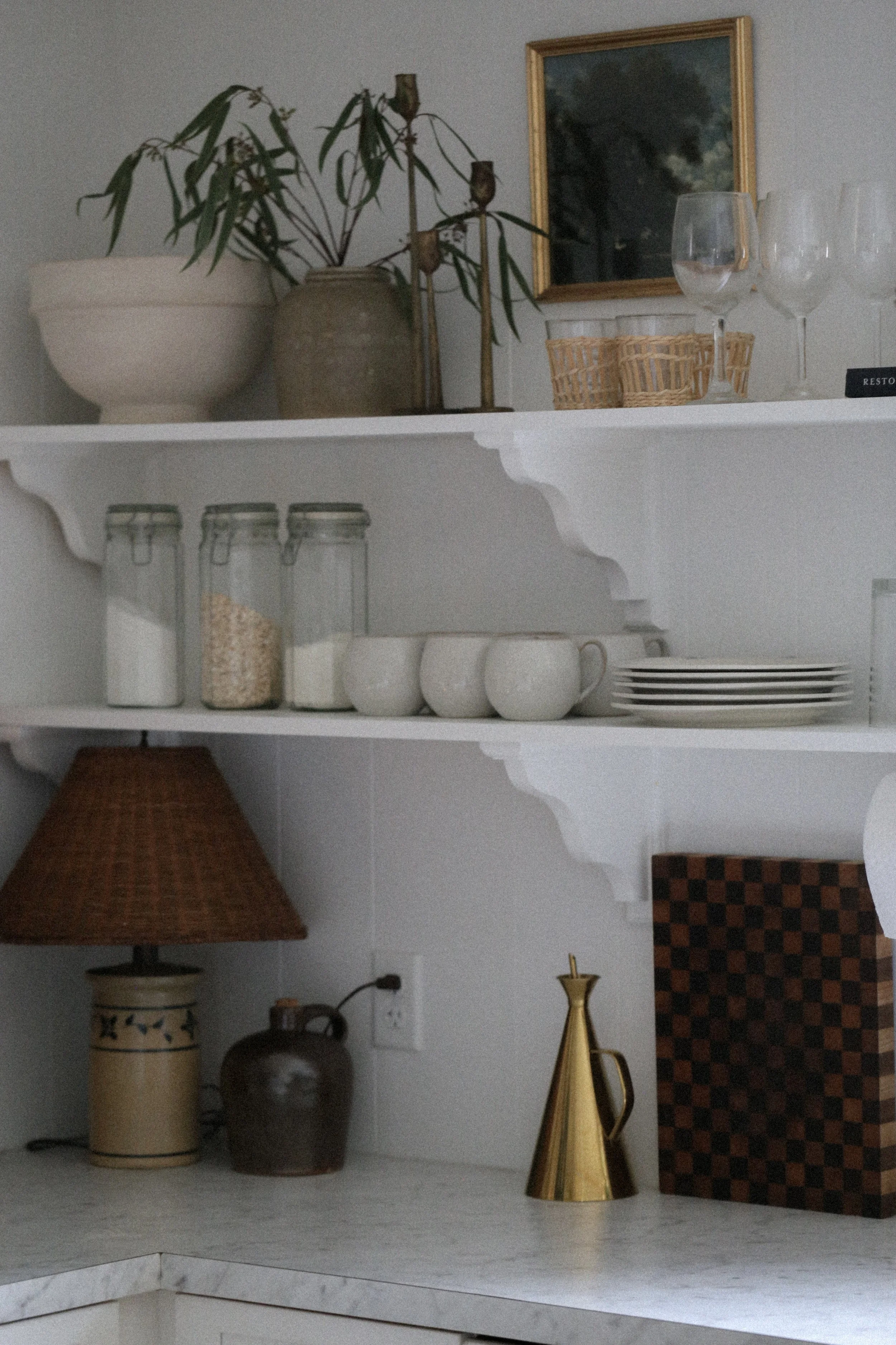 White kitchen open shelving with antique lamp on countertop, glass canisters, dinnerware.