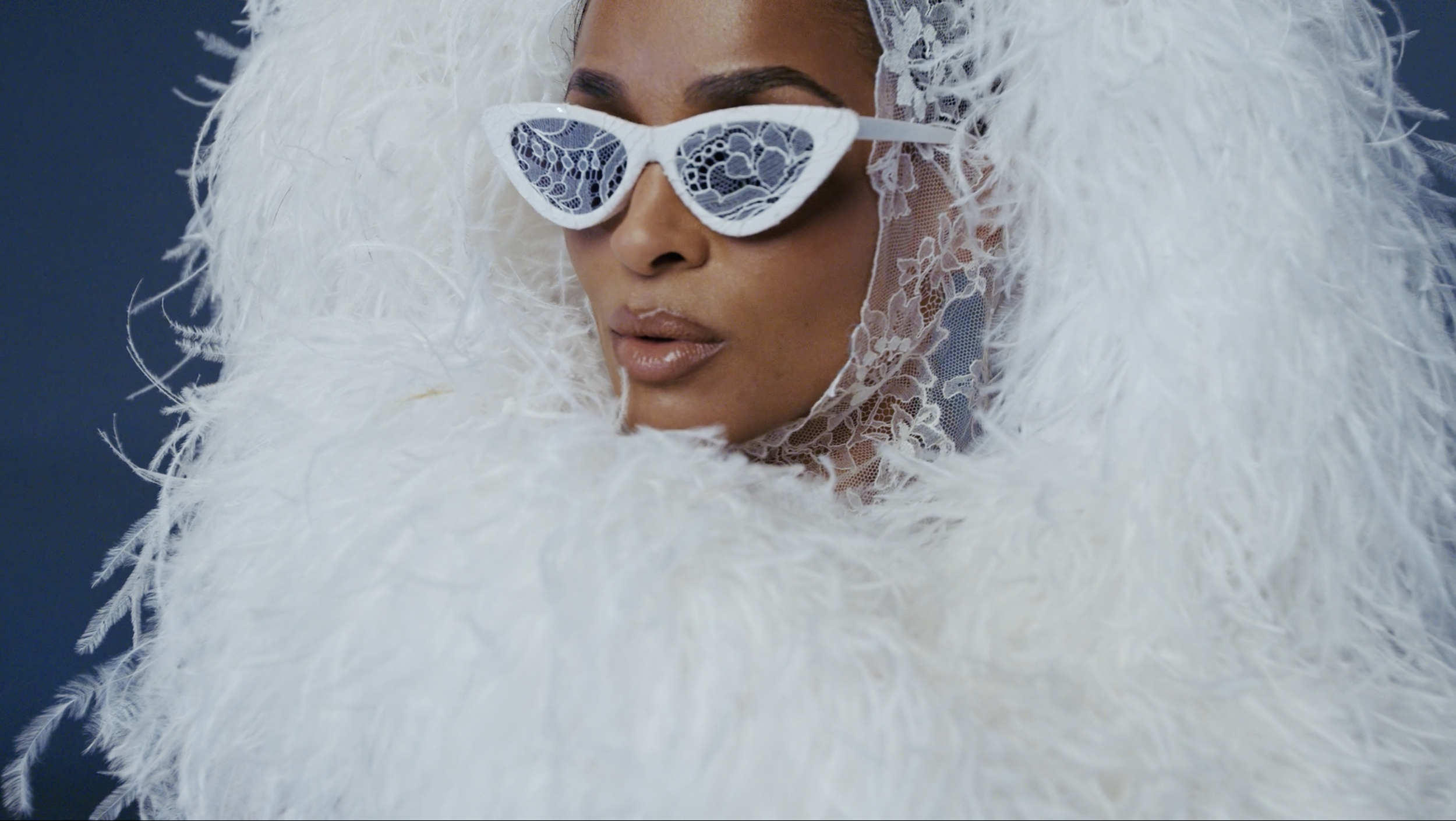 A woman wearing white lace sunglasses and a white feathered headdress with lace details.