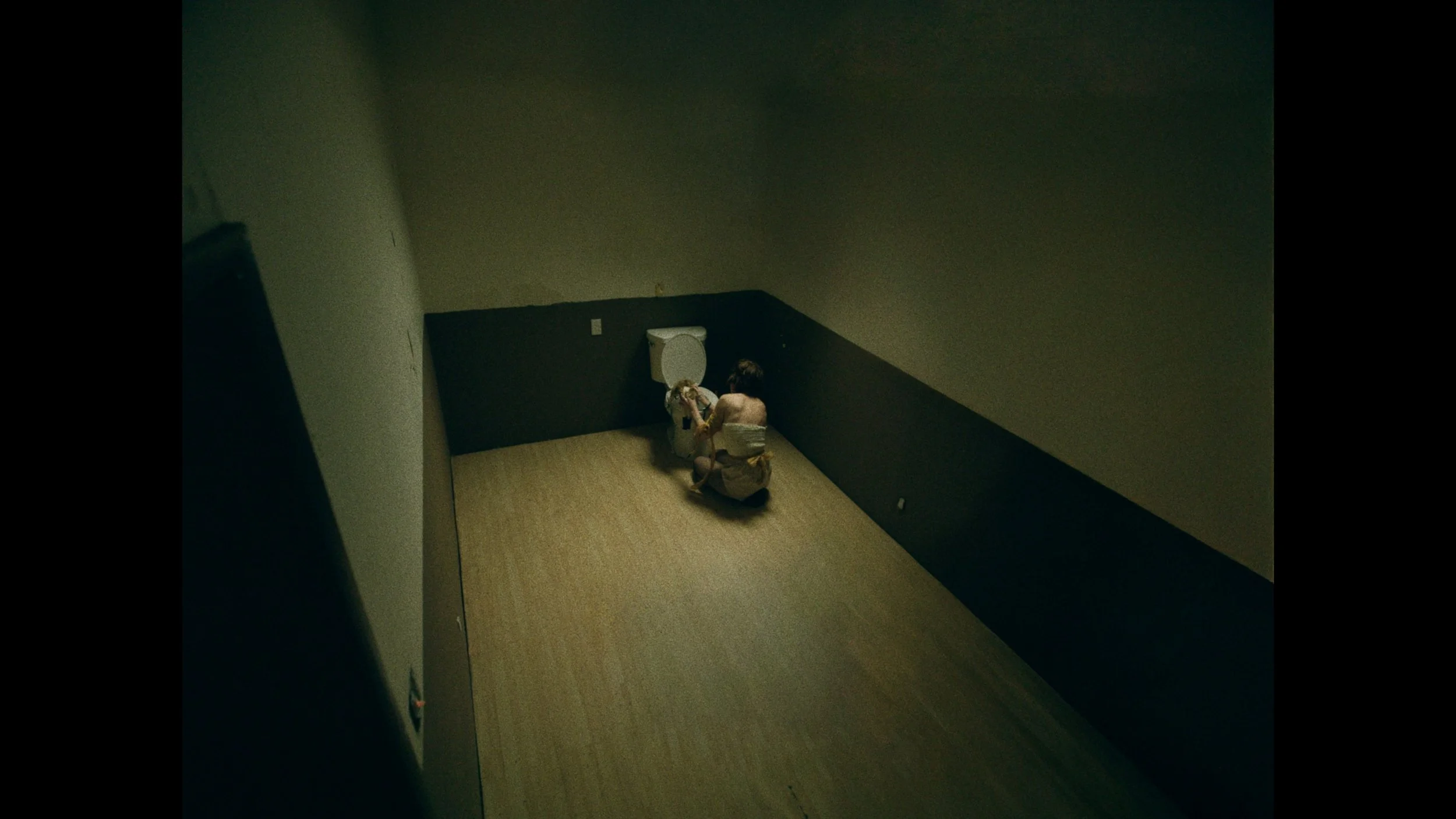 A person sitting on the floor in an empty room with a toilet, viewed from above.