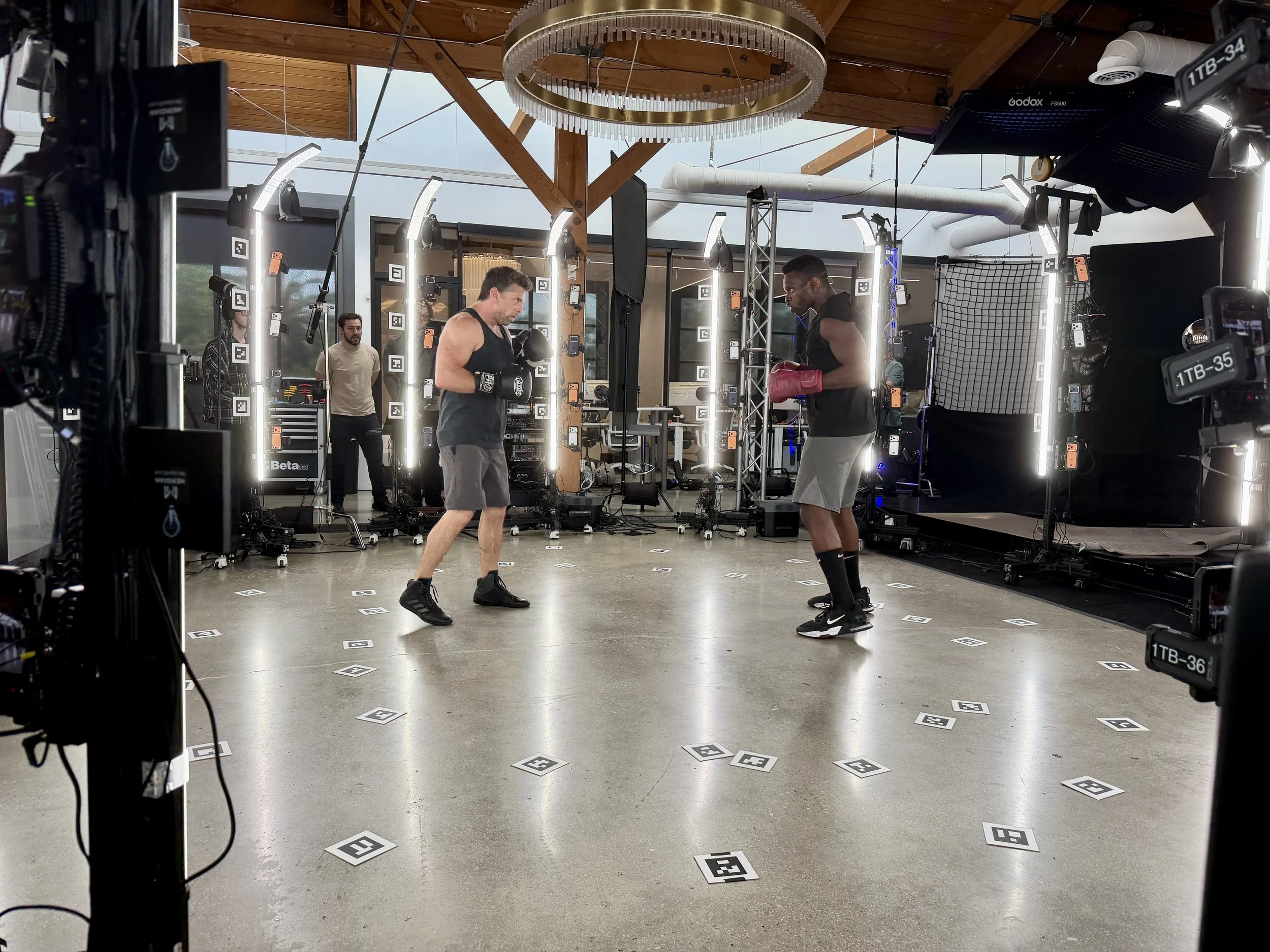 Two men in athletic gear boxing in a gym or studio with lighting equipment and cameras around them. Meridian 4D portable volumetric gaussian splat system