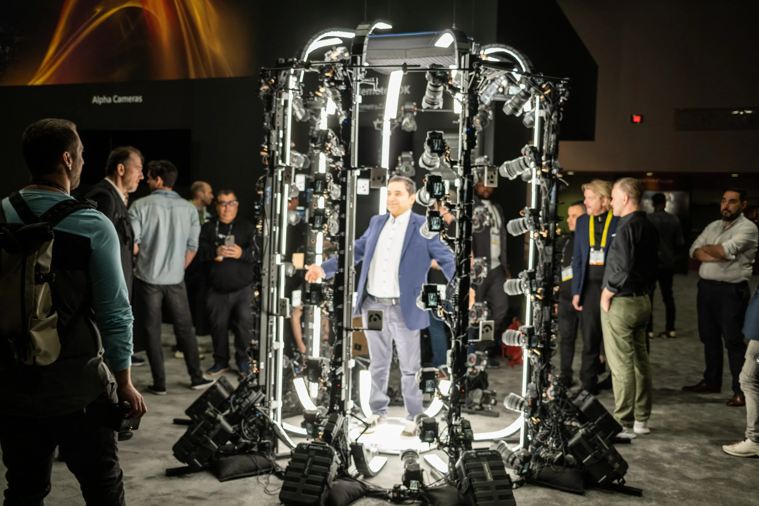 A group of people gathered around a circular lighting rig at a technology or trade show, with a man standing at the center smiling.