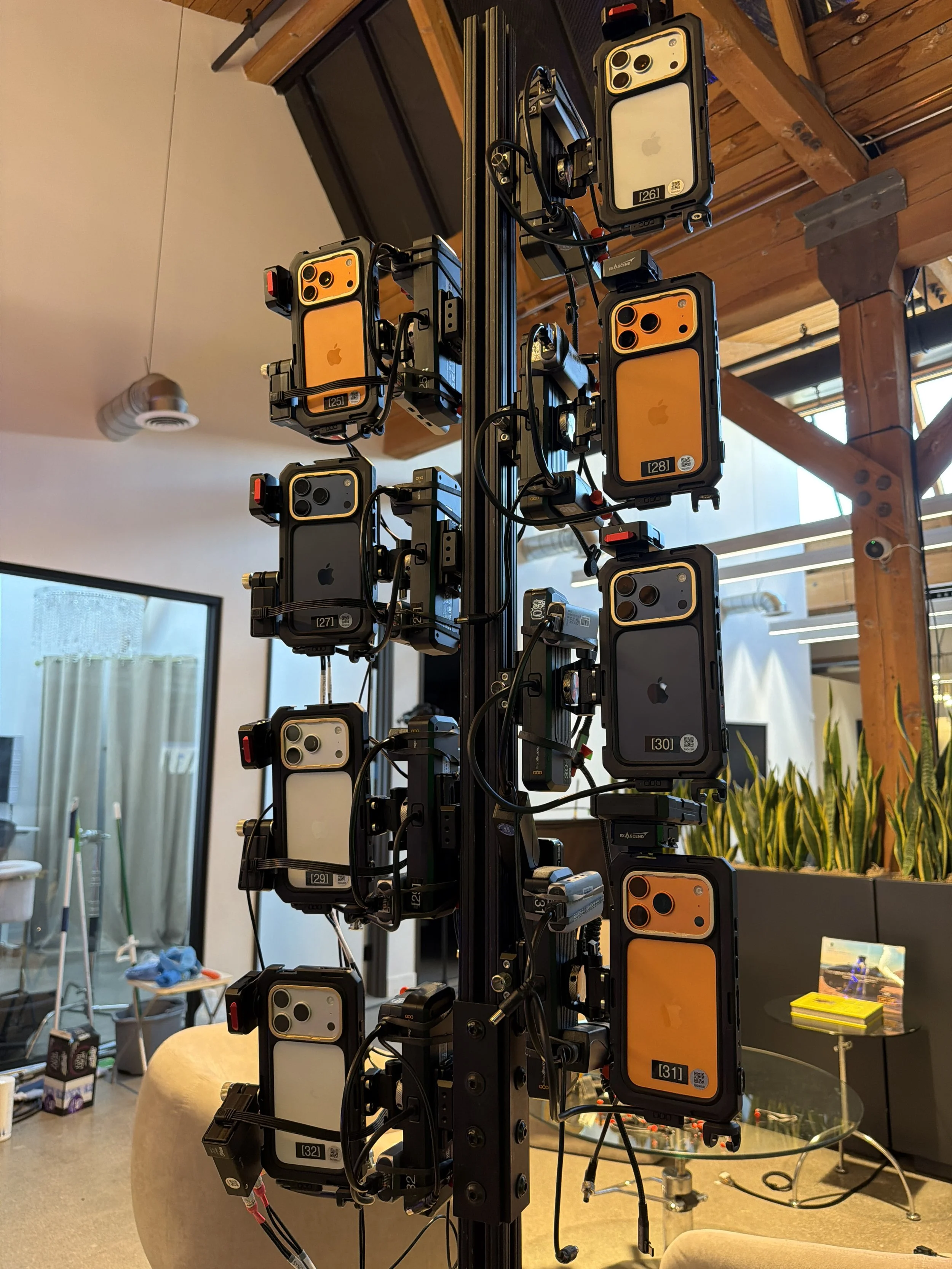 A vertical black metal structure with multiple orange and black camera-like devices mounted on it, inside a room with a wooden ceiling, lMeridian 4D portable volumetric gaussian splat system