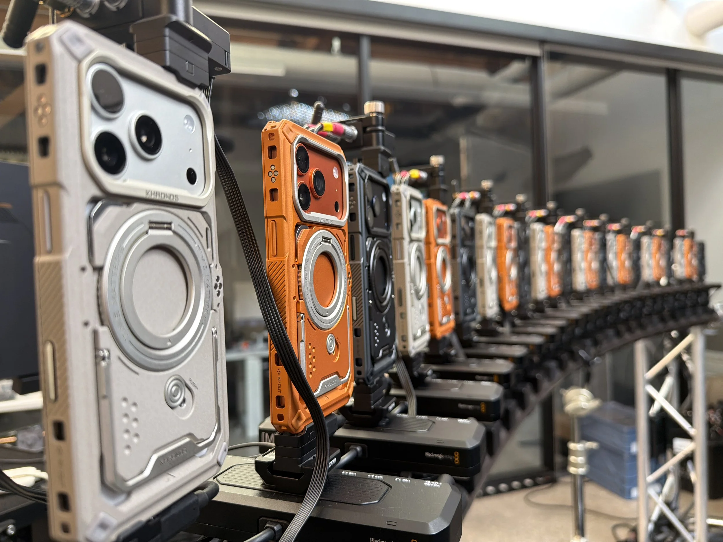 A rack of various handheld radios and communication devices, with the focus on an orange radio in the foreground, and other radios in different colors lined up on the shelf.