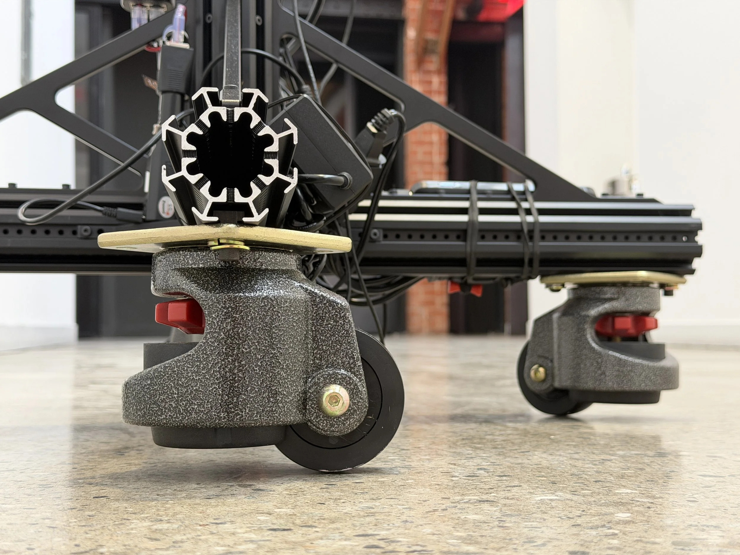 Close-up view of the wheels and structural components of a 3D printers or CNC machine, including black metal frame, wiring, and support pads on Meridian 4D portable volumetric gaussian splat system