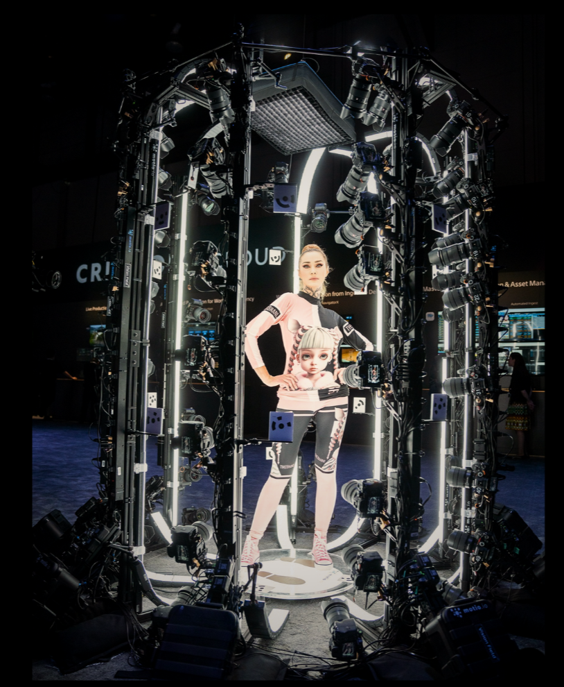 A woman standing inside a complex camera rig, with multiple cameras and lighting equipment surrounding her. The backdrop features a large digital screen displaying animated characters.