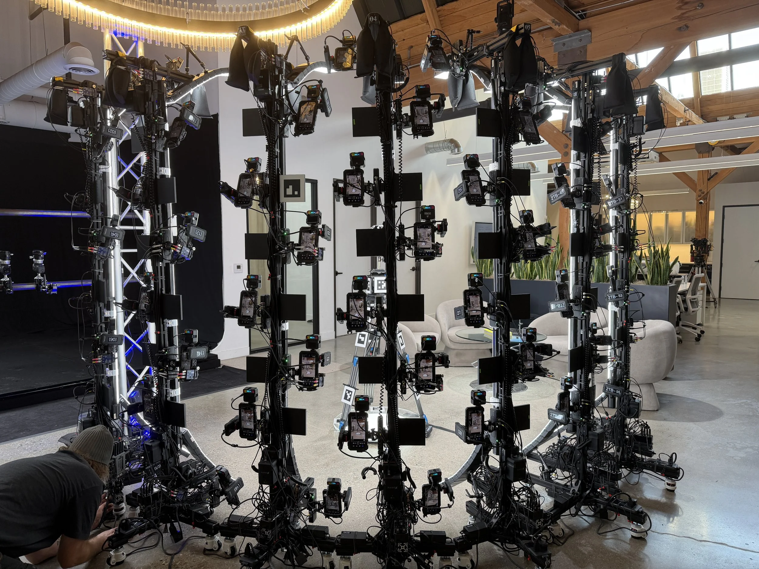 An indoor space with a large, circular lighting fixture on the ceiling. The room contains a complex setup of numerous cameras and equipment Meridian 4D portable volumetric gaussian splat system