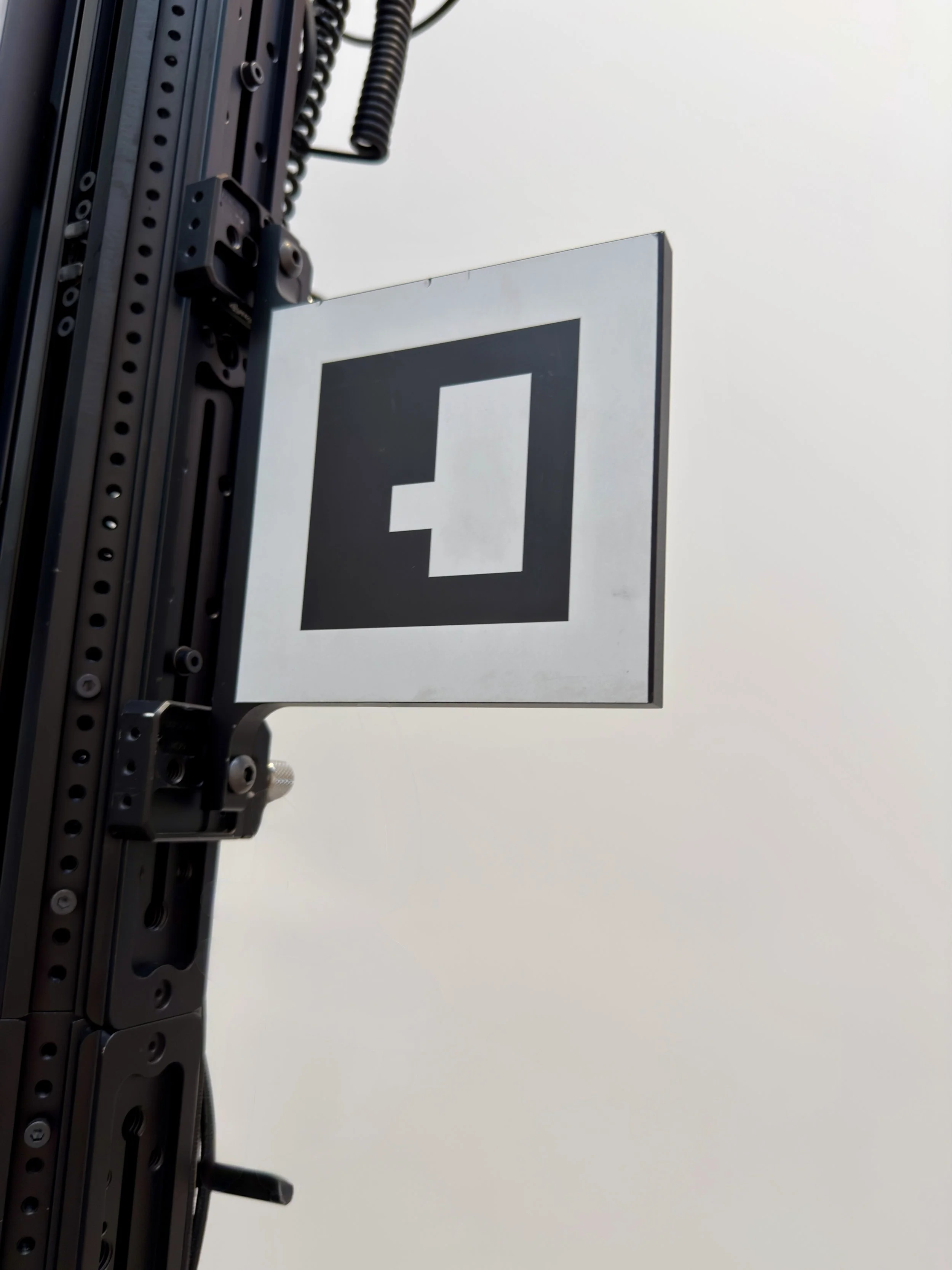Close-up of a mechanical support structure with a sign displaying a black square with a white outline and a smaller black square in the center, against a cloudy sky