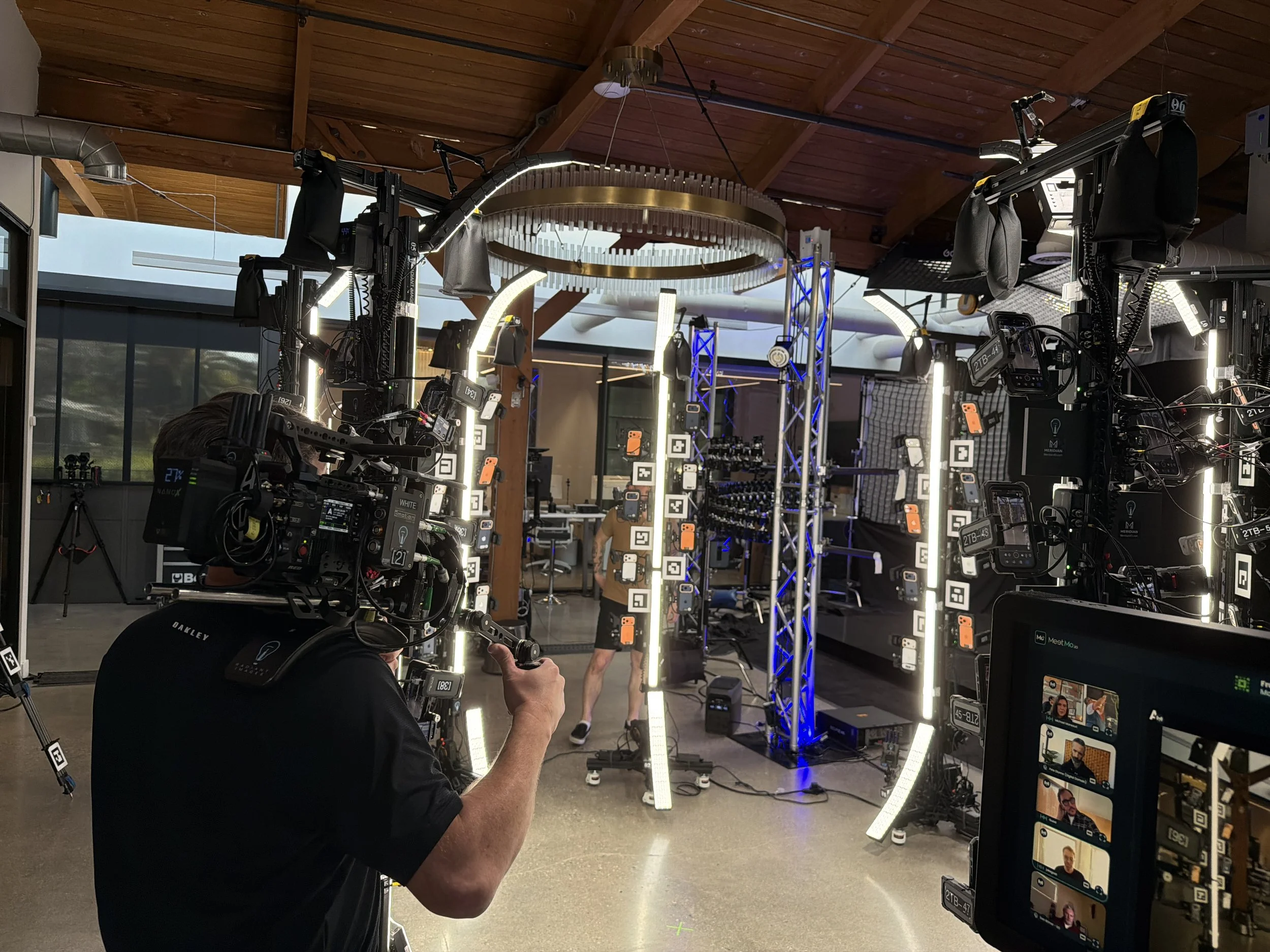 Music studio with cameras, lighting, and a person filming a person walking through a modern setup with digital screens and lighting fixtures. Meridian 4D portable volumetric gaussian splat system