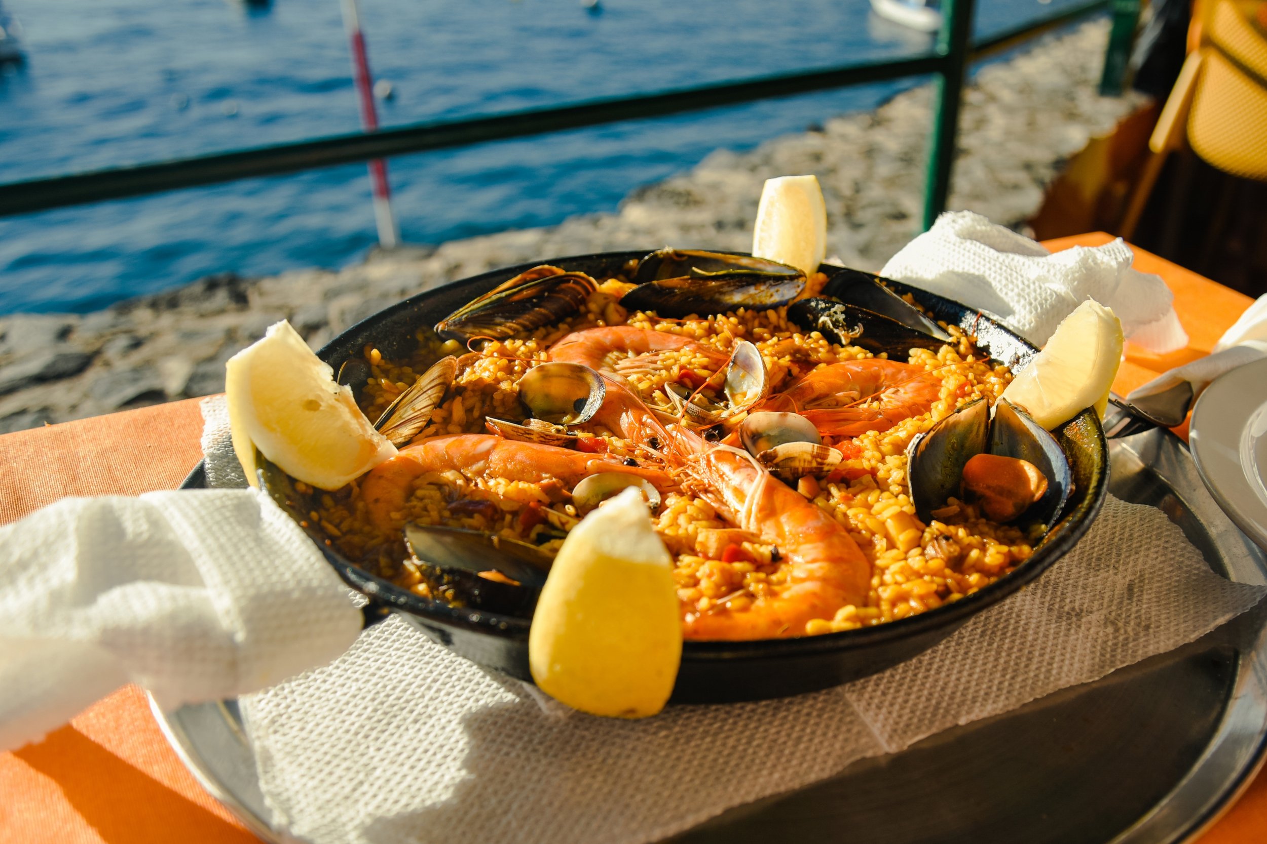 Paella de mariscos con camarones, mejillones y limón en una mesa junto a la playa.
