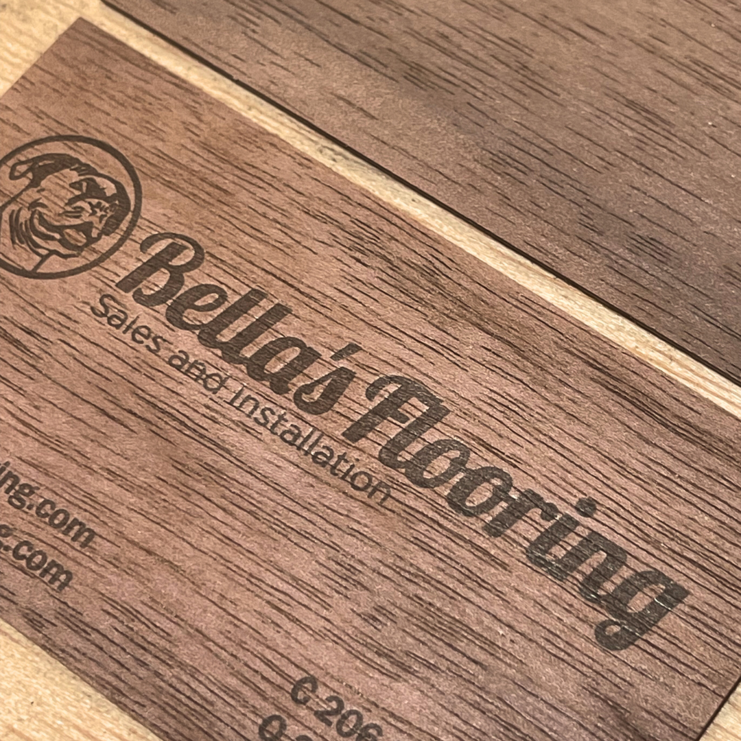 Close-up of a wooden surface with the Bellacio logo and text engraved, featuring a lion head emblem and website links.
