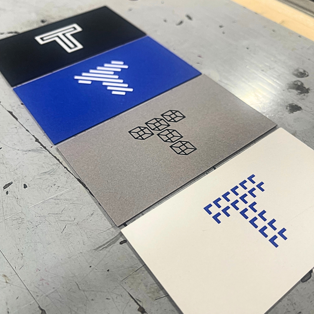 Four color swatches with geometric and logo designs, arranged on a gray surface.