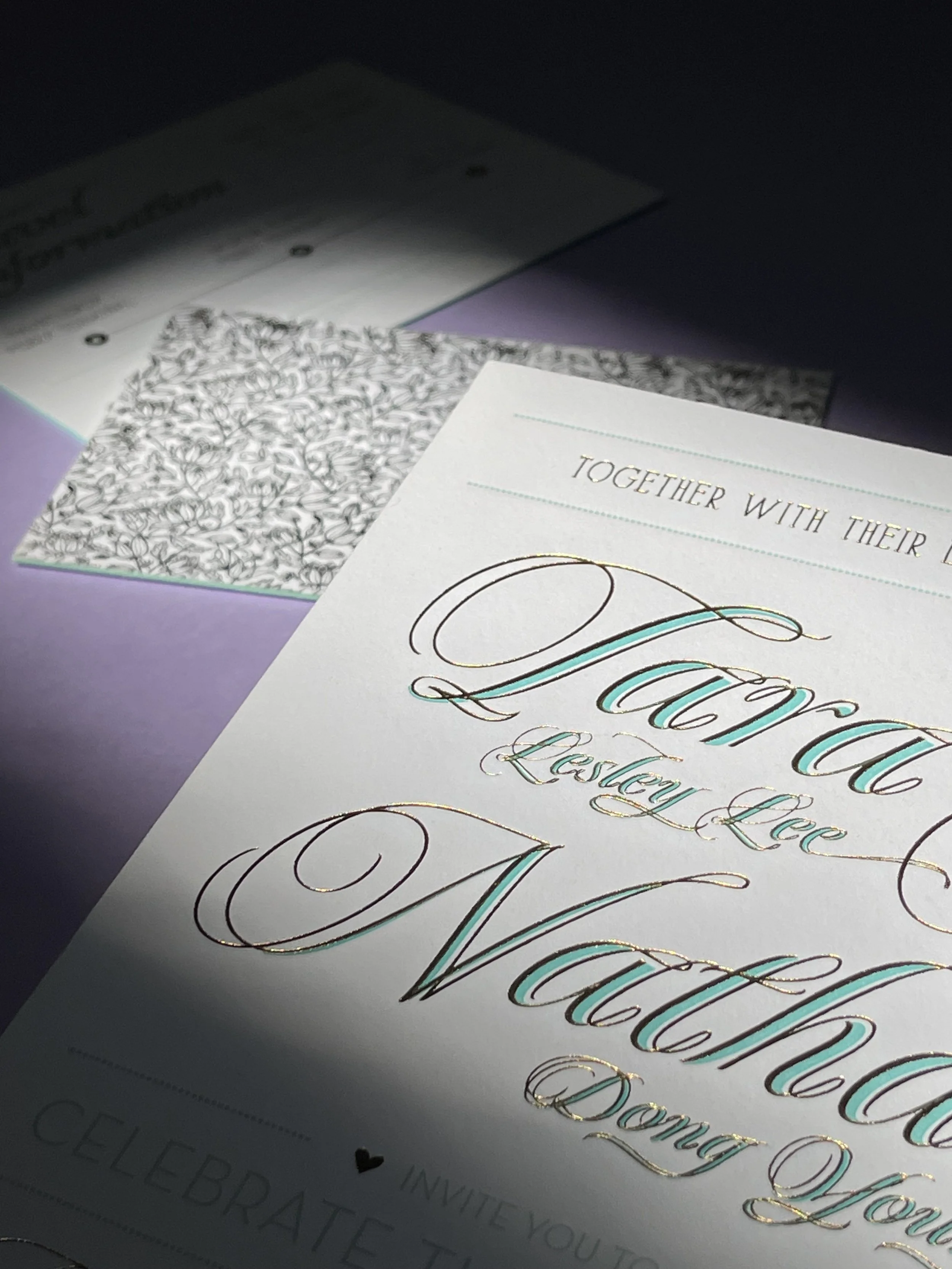 Close-up of wedding invitation cards with elegant calligraphy, with one card reading: Together with their 0
0Flor  Lee Lee 
nd Wart and, Doney Lee. The cards feature decorative floral and ornate designs, with gold and pastel accents.
