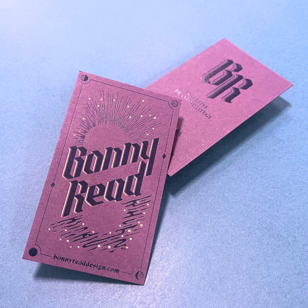Two pink paper cards with laser-cut designs, one showing a sunrise reflection on water with the words "Carry Read" and the other with a geometric logo and the text "Creative Digital Strategy".