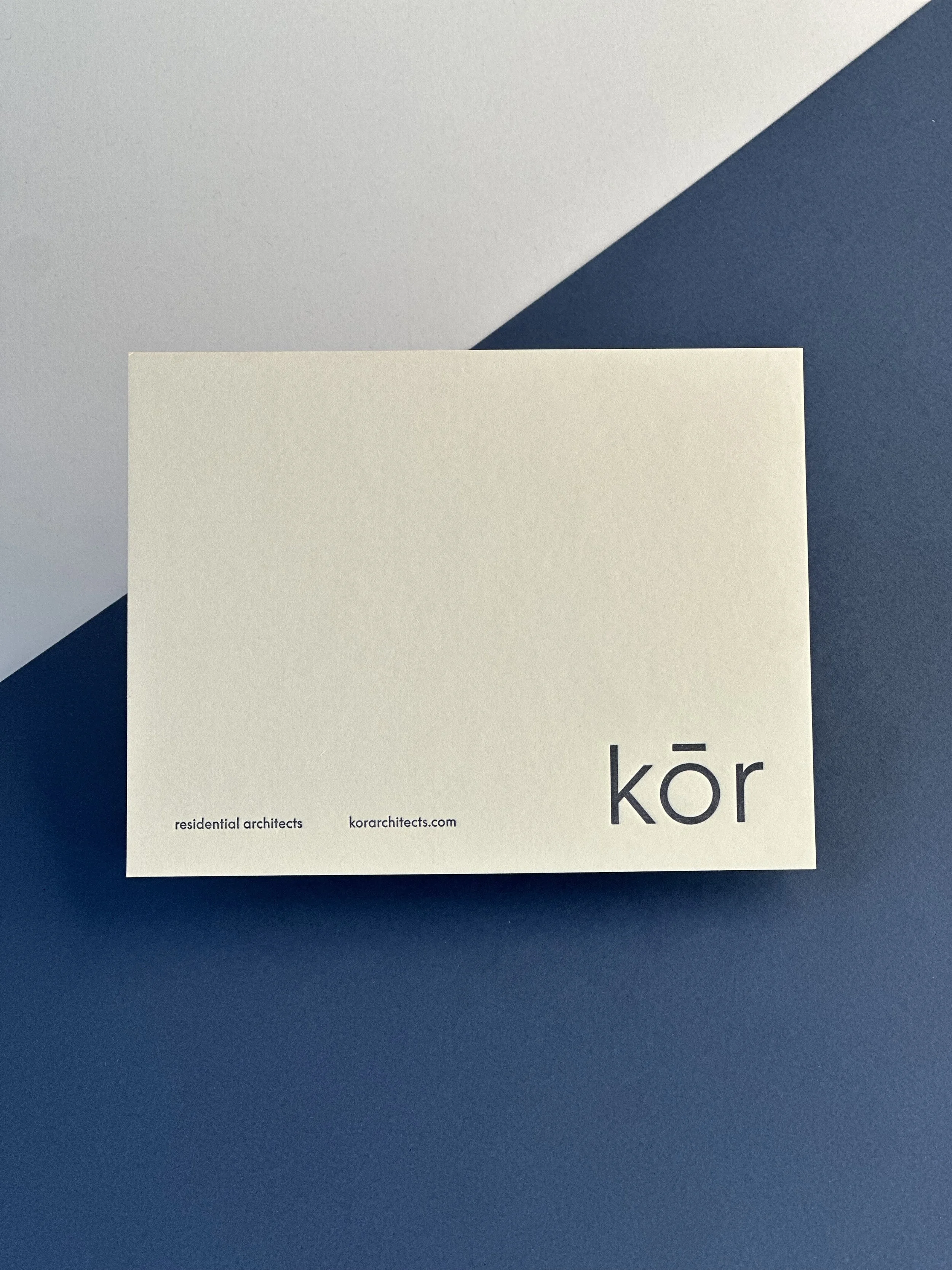 A white business card with the word 'kōr' and a dot above the 'o' in black text, placed on a blue surface with a light gray background.
