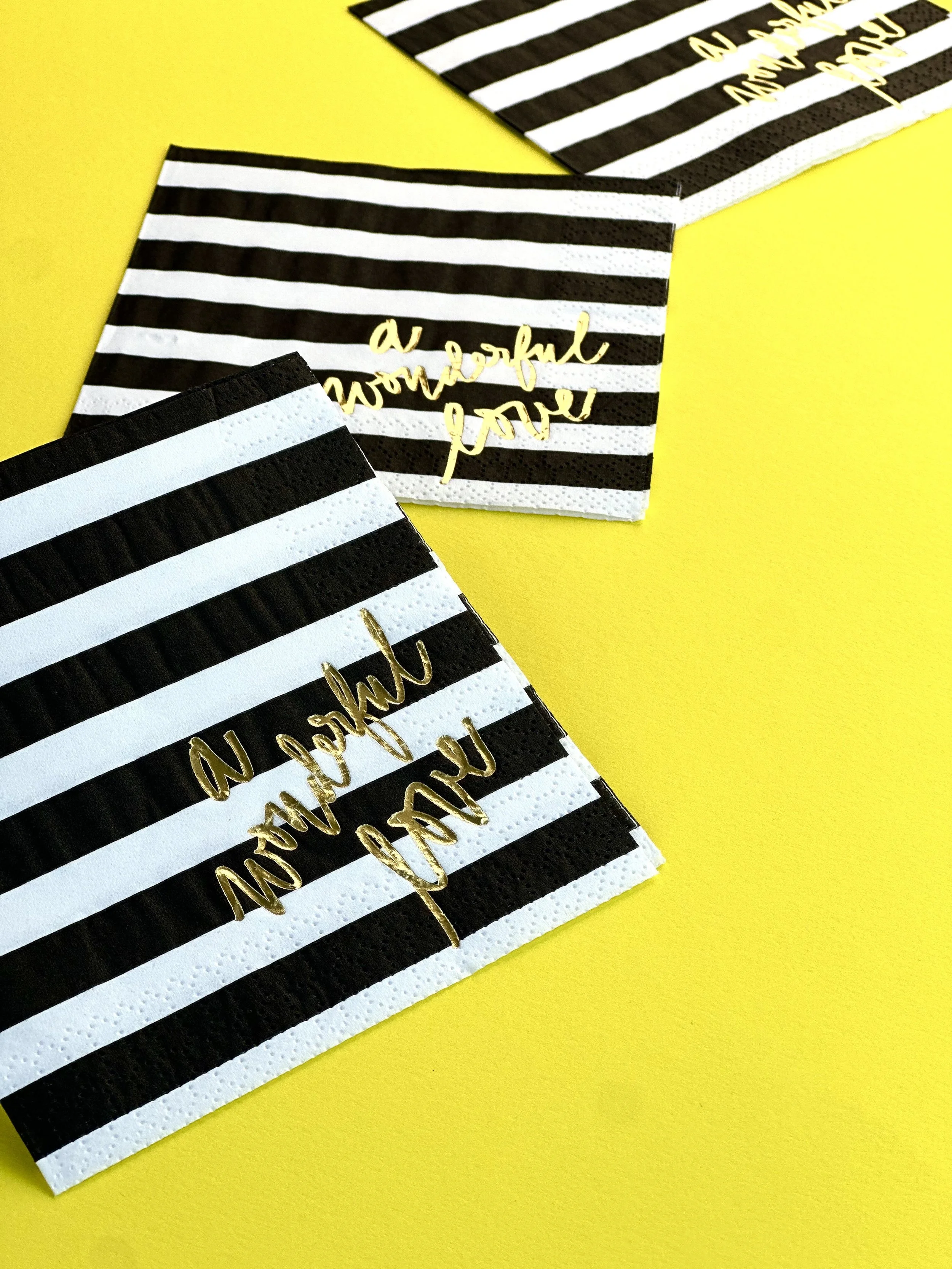 Set of black and white striped paper napkins with gold foil text that says 'a wonderful you,' on a bright yellow background.