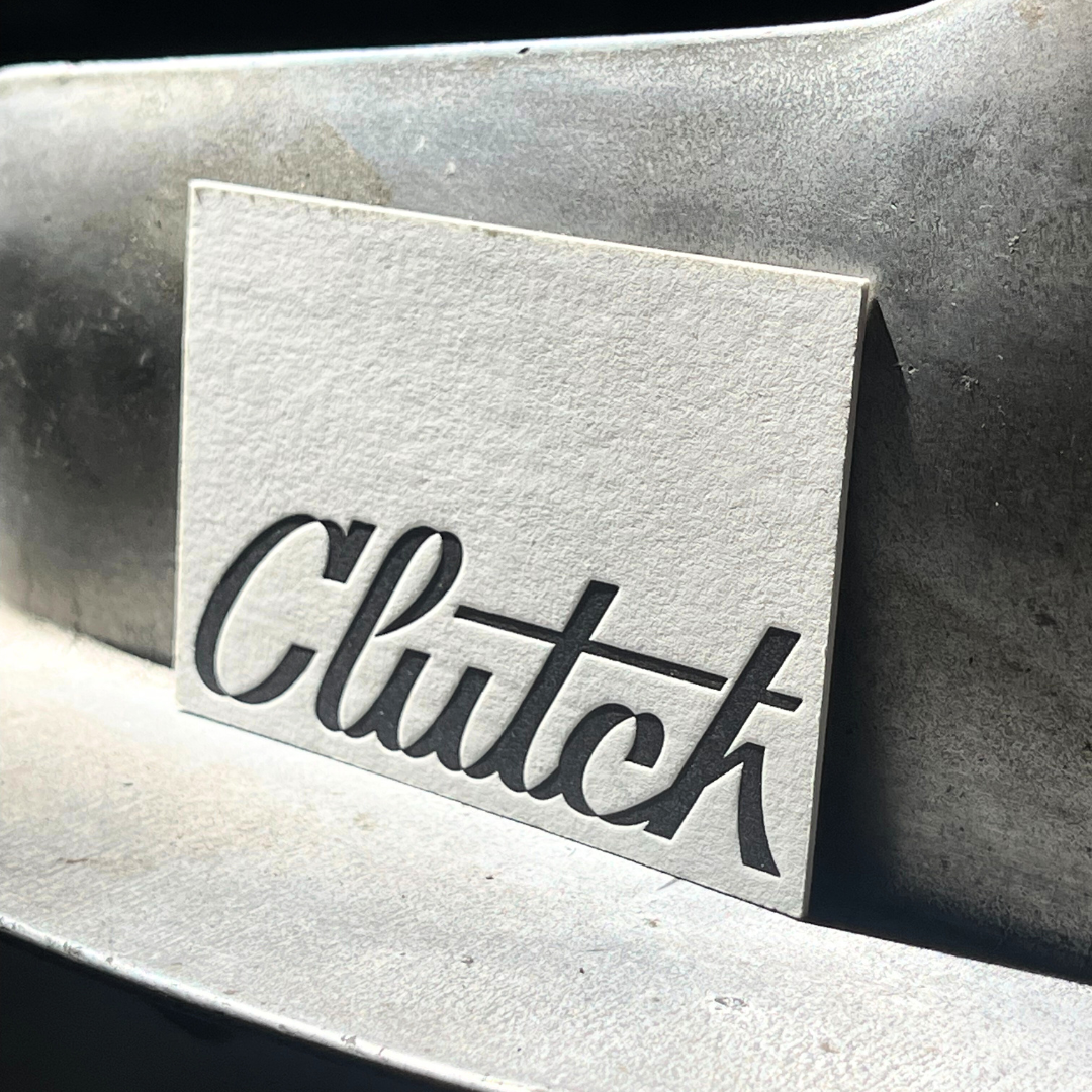 Close-up of a metallic surface with a white rectangular label that has the word 'Clutch' cut out in black letters.