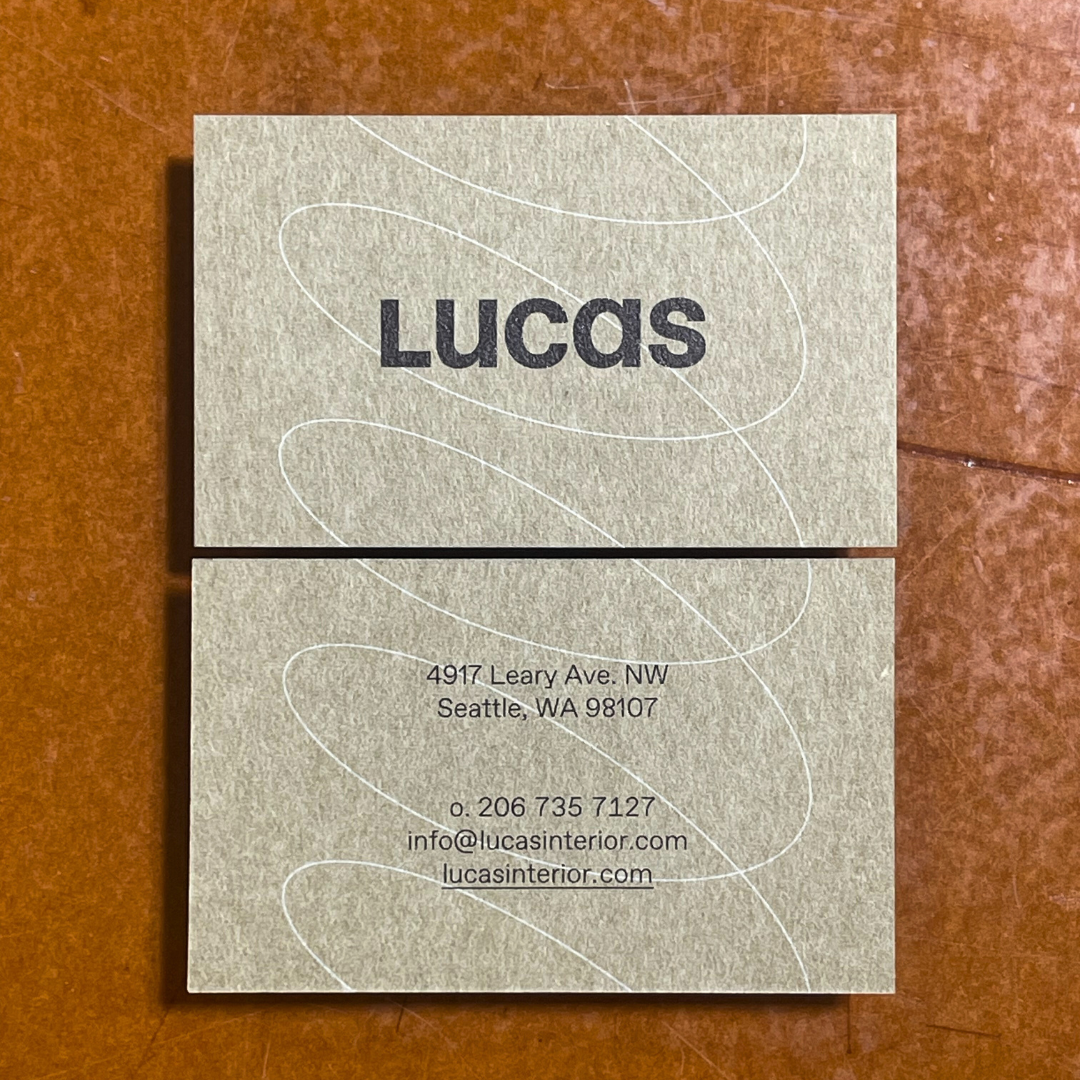 Business card for Lucas, with the address 4917 Leary Ave. NW, Seattle, WA 98107 and contact info including phone number and email, on a textured beige background with white swirl design.