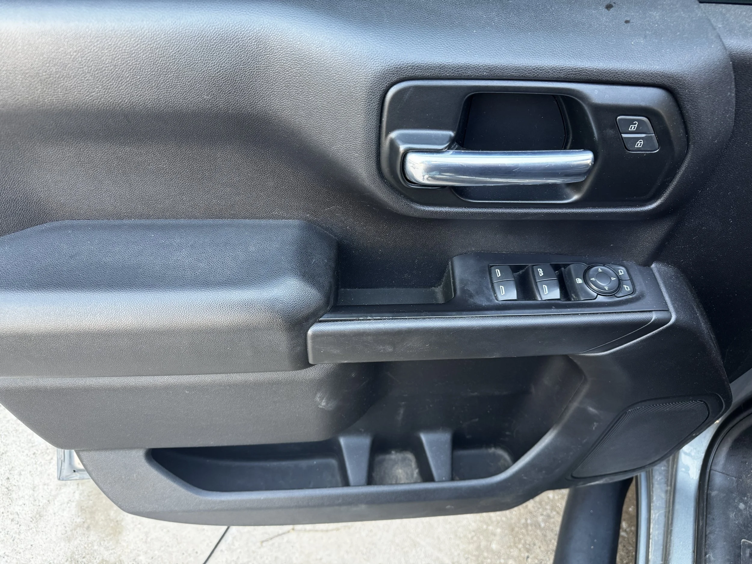 Interior of a vehicle door panel with a silver door handle, lock/unlock buttons, and window control switches.