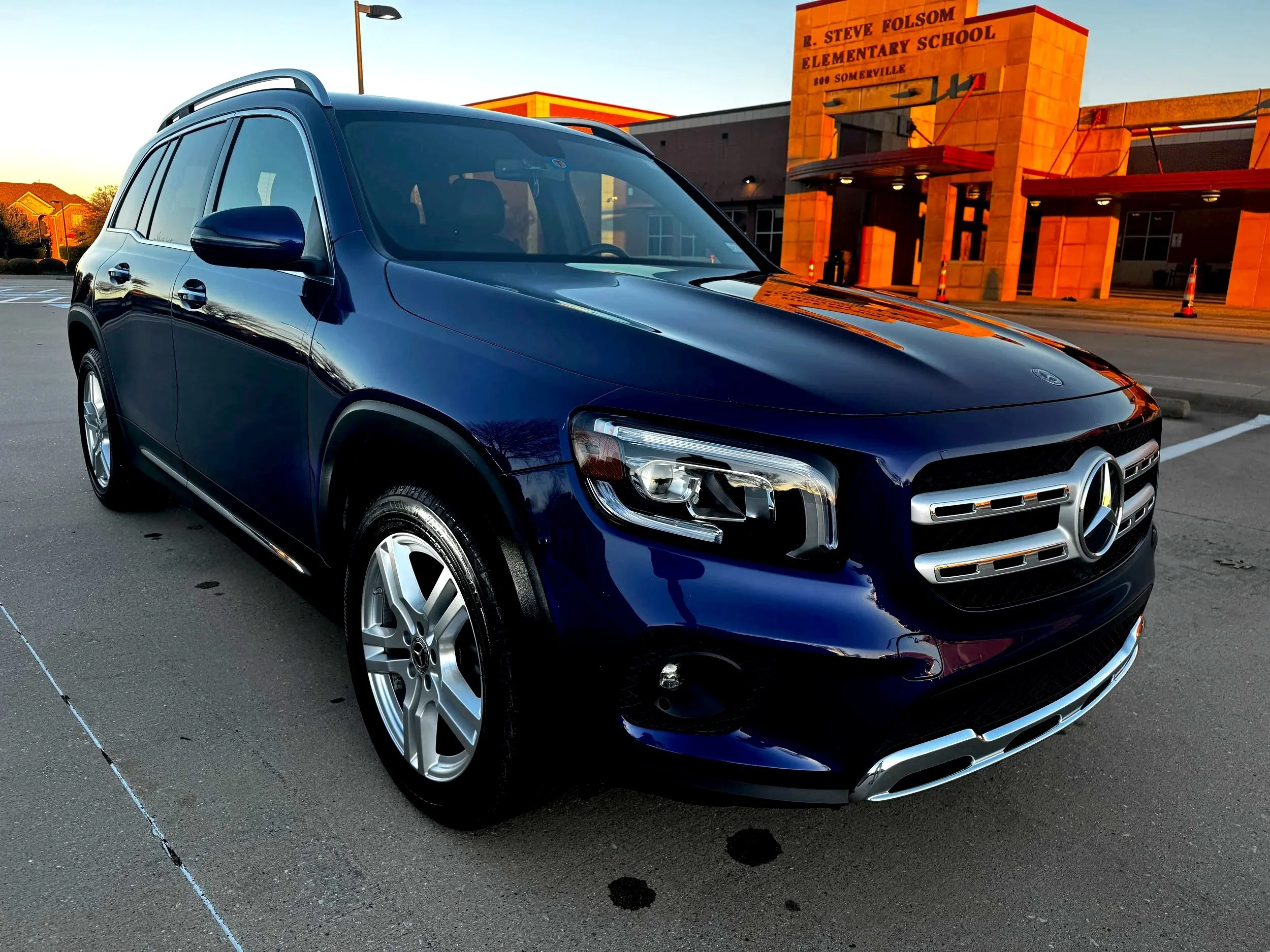 A dark blue Mercedes-Benz SUV parked in front of R. Steve Folsom Elementary School during sunset.