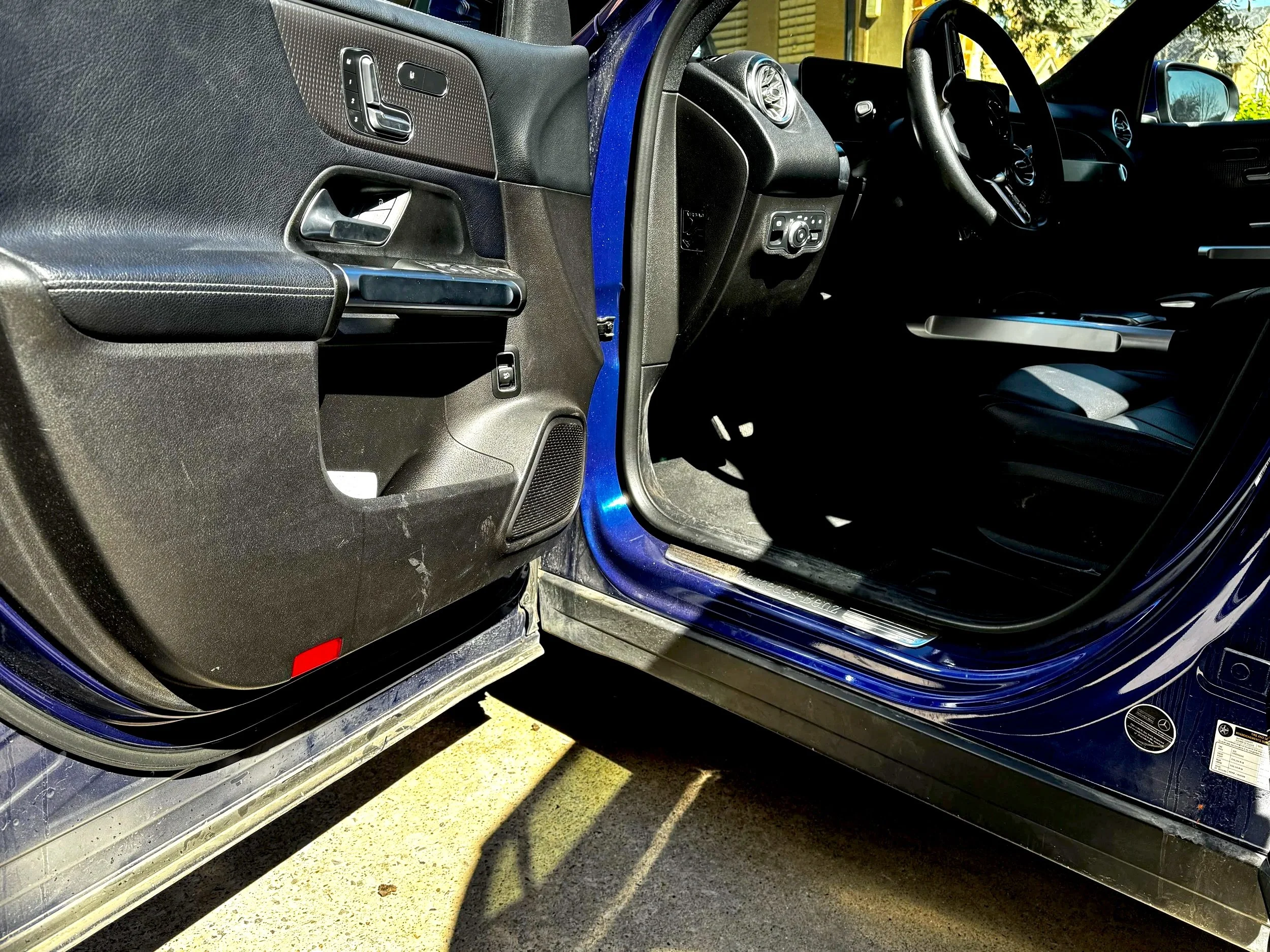 The image shows the open door of a blue vehicle, revealing the driver's side interior, including the steering wheel, dashboard, and driver's seat.