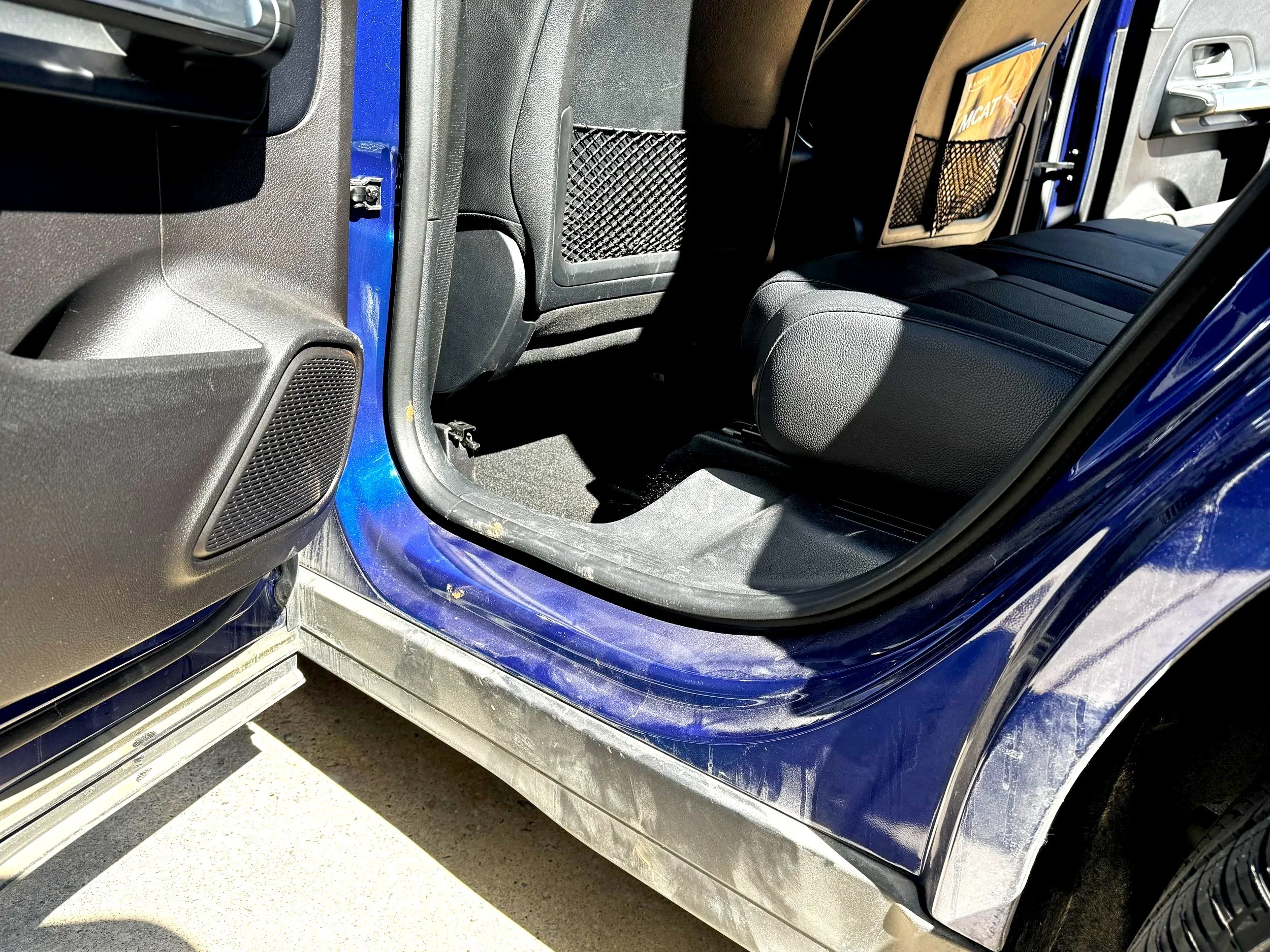 The interior of a blue vehicle showing the rear passenger seat area, with black seats, door panel, and storage pouches on the back of front seats.