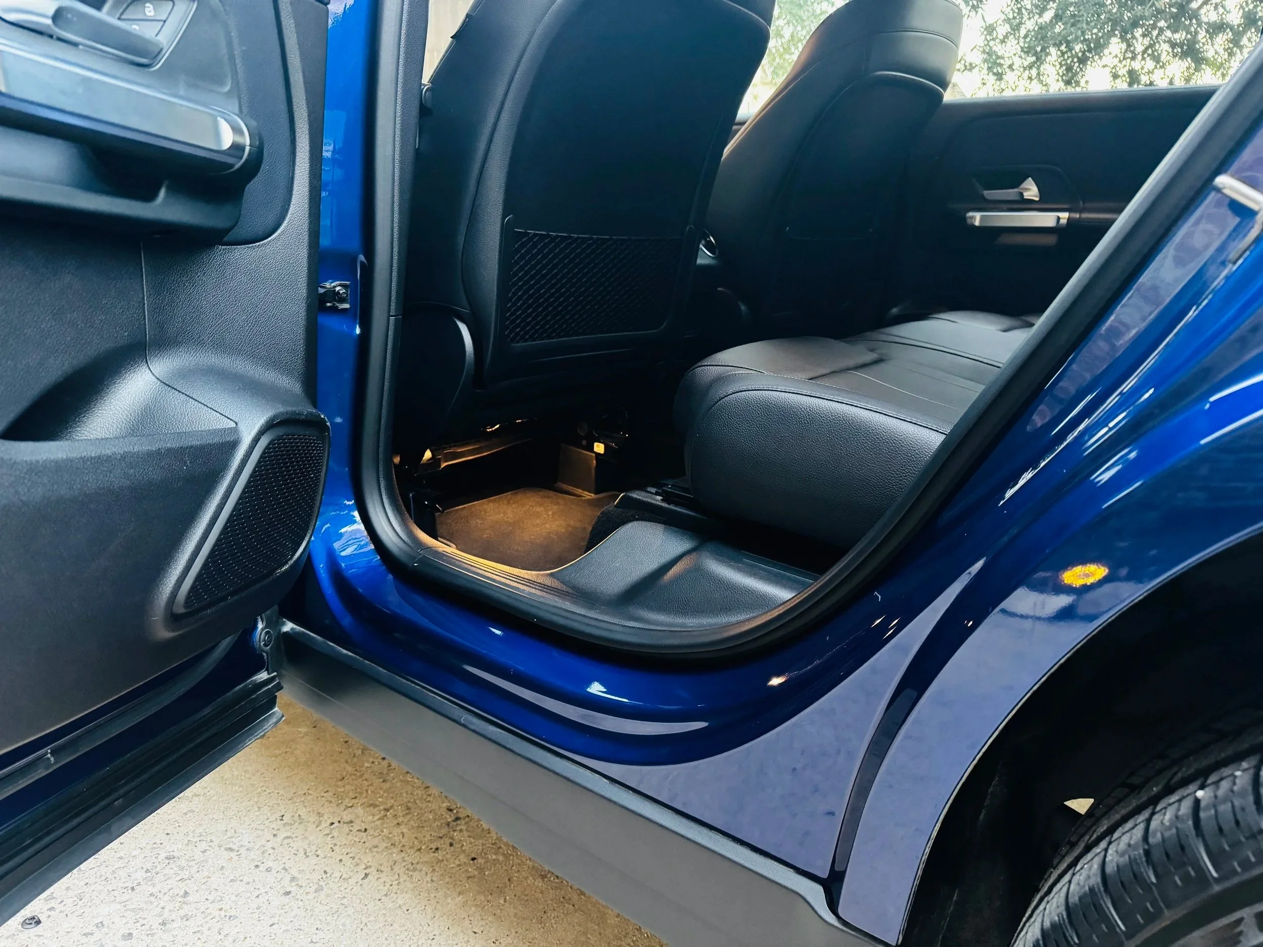 Interior view of a blue car showing the front passenger seat and the back seat, with the passenger door open.