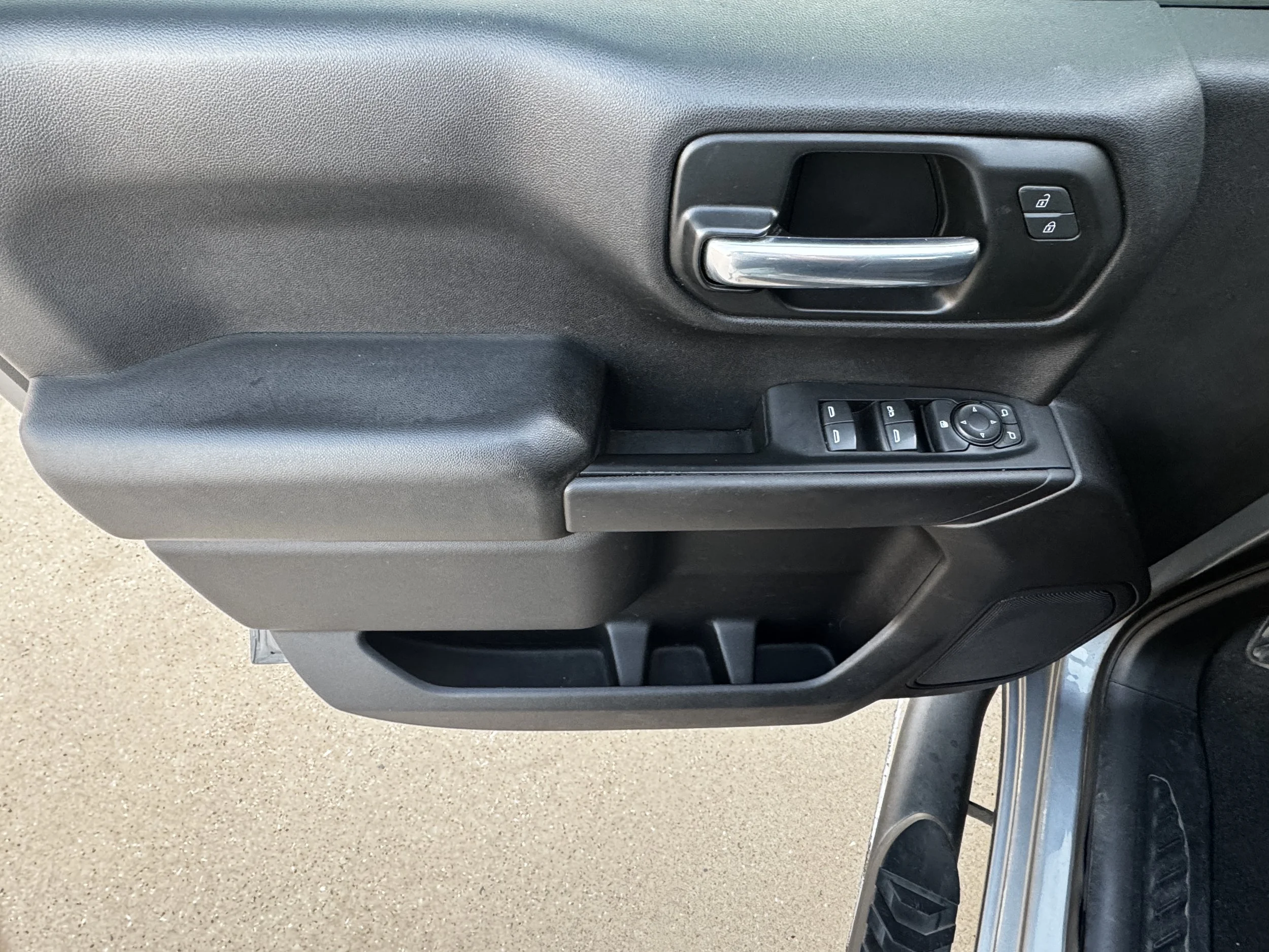 Close-up of a car door interior showing a silver door handle, lock/unlock buttons, window controls, and side mirror adjustment control.